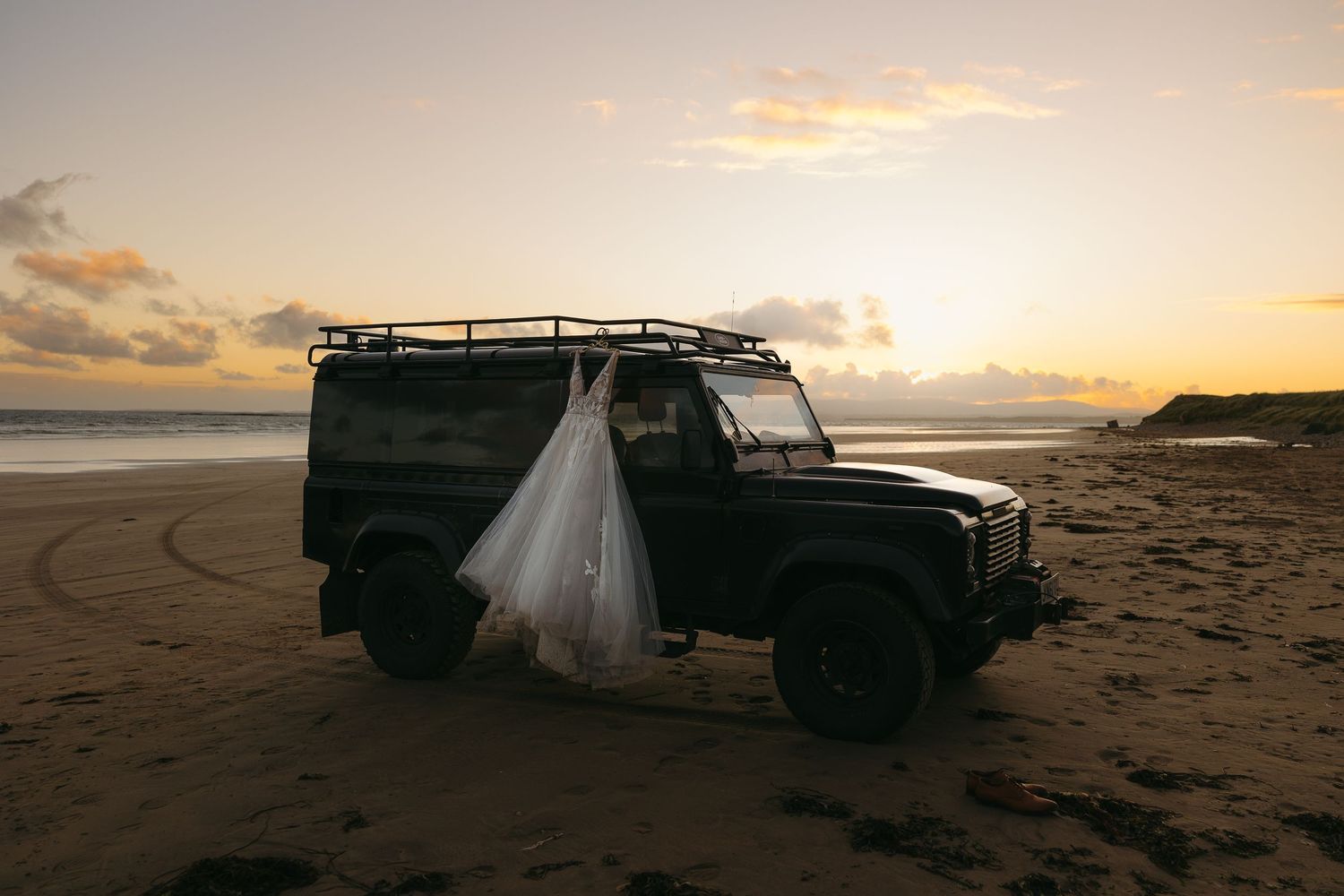 Wedding couple posing with vintage car on beach at golden hour.