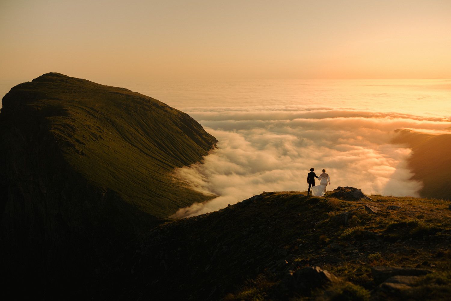 Silhouettes against a golden sunset sky on a mountain ridge above clouds.