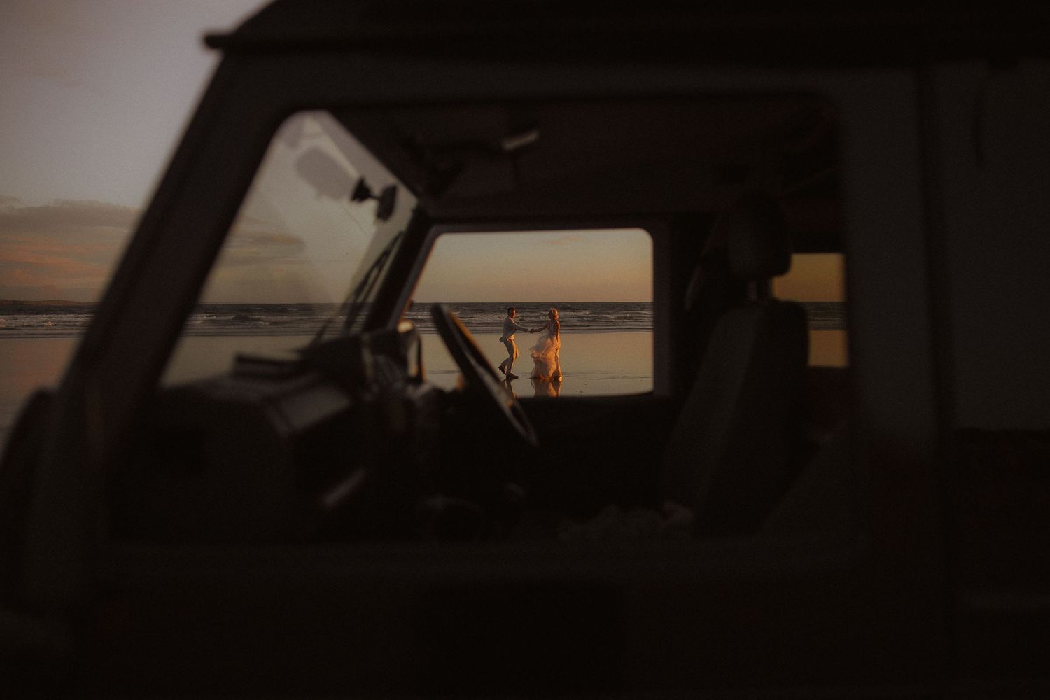 Sunset silhouette viewed through car window frame at beach.