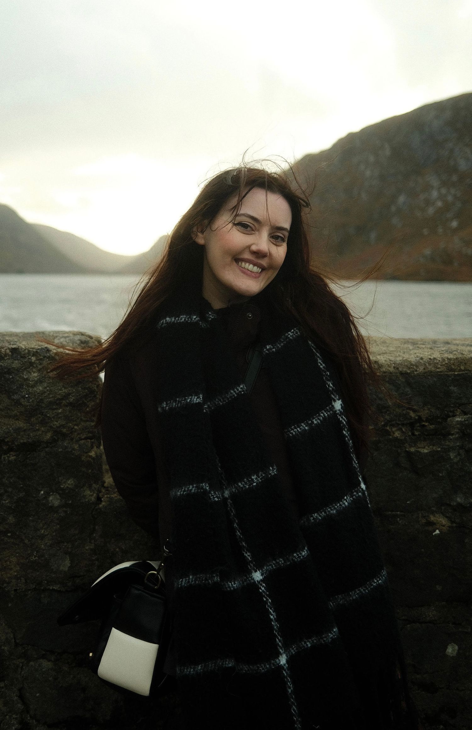 Scenic portrait by a mountain lake with dark winter fashion.