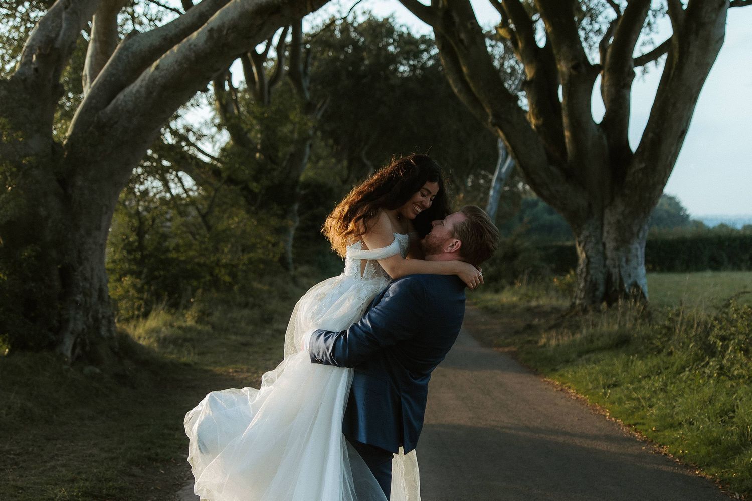 A romantic wedding moment captured under large trees at golden hour.