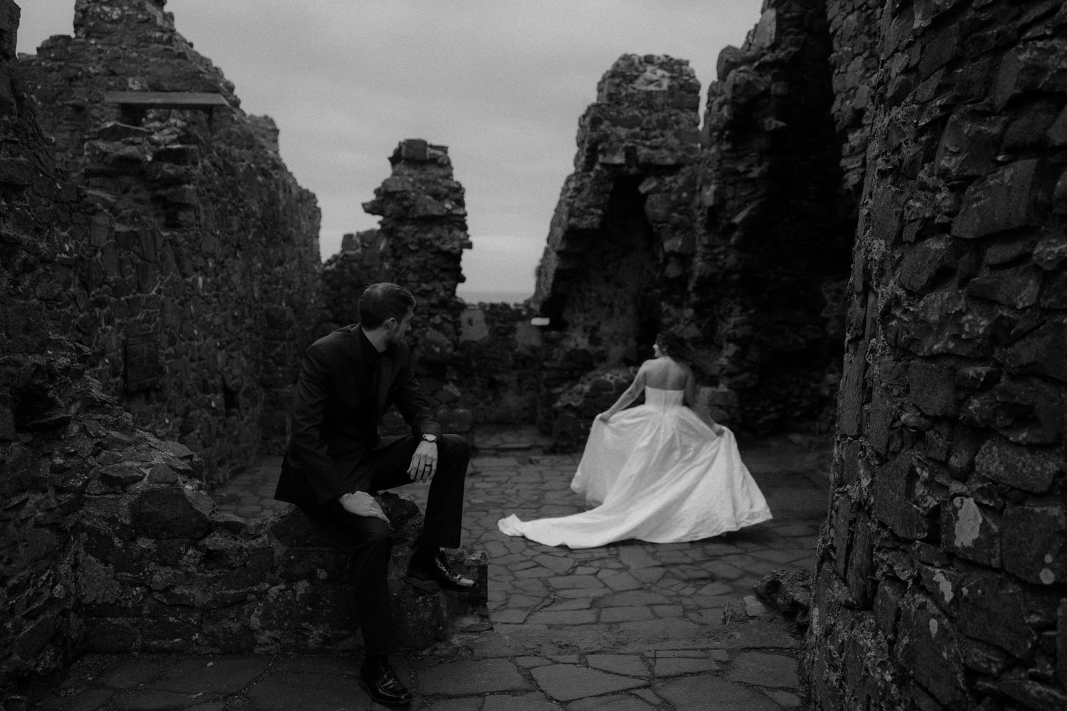 Black and white photo of bride and groom posing among ancient stone ruins on their wedding day.