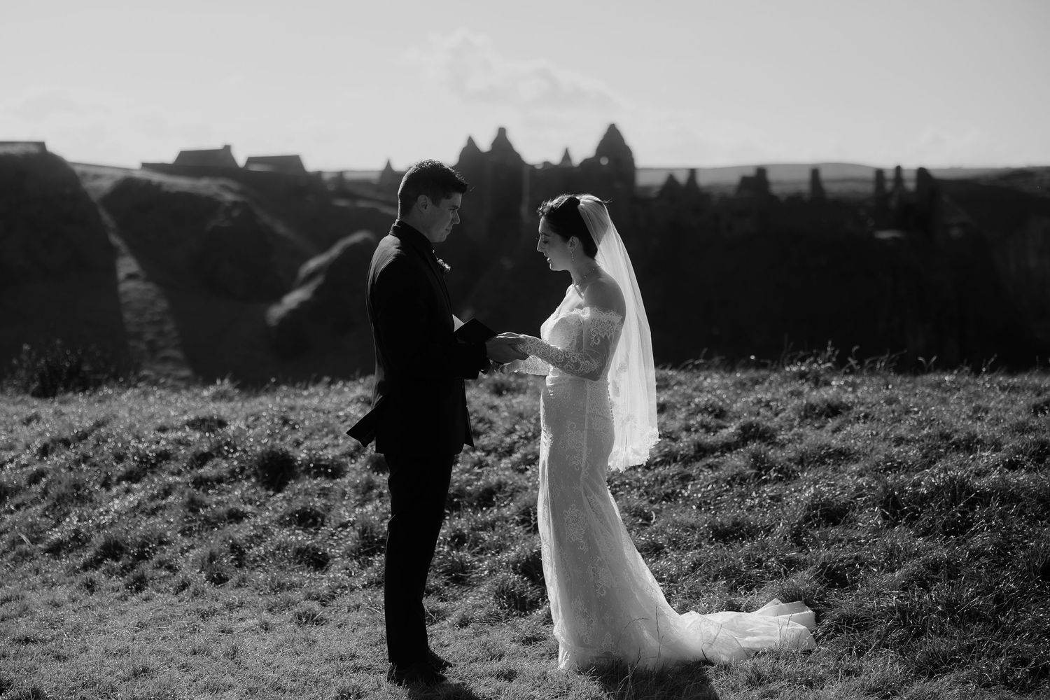 Black and white photo of couple exchanging vows on grassy hilltop.