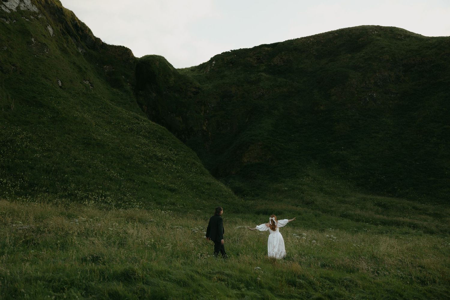 Rolling green hills and mountains with couple walking in distance.