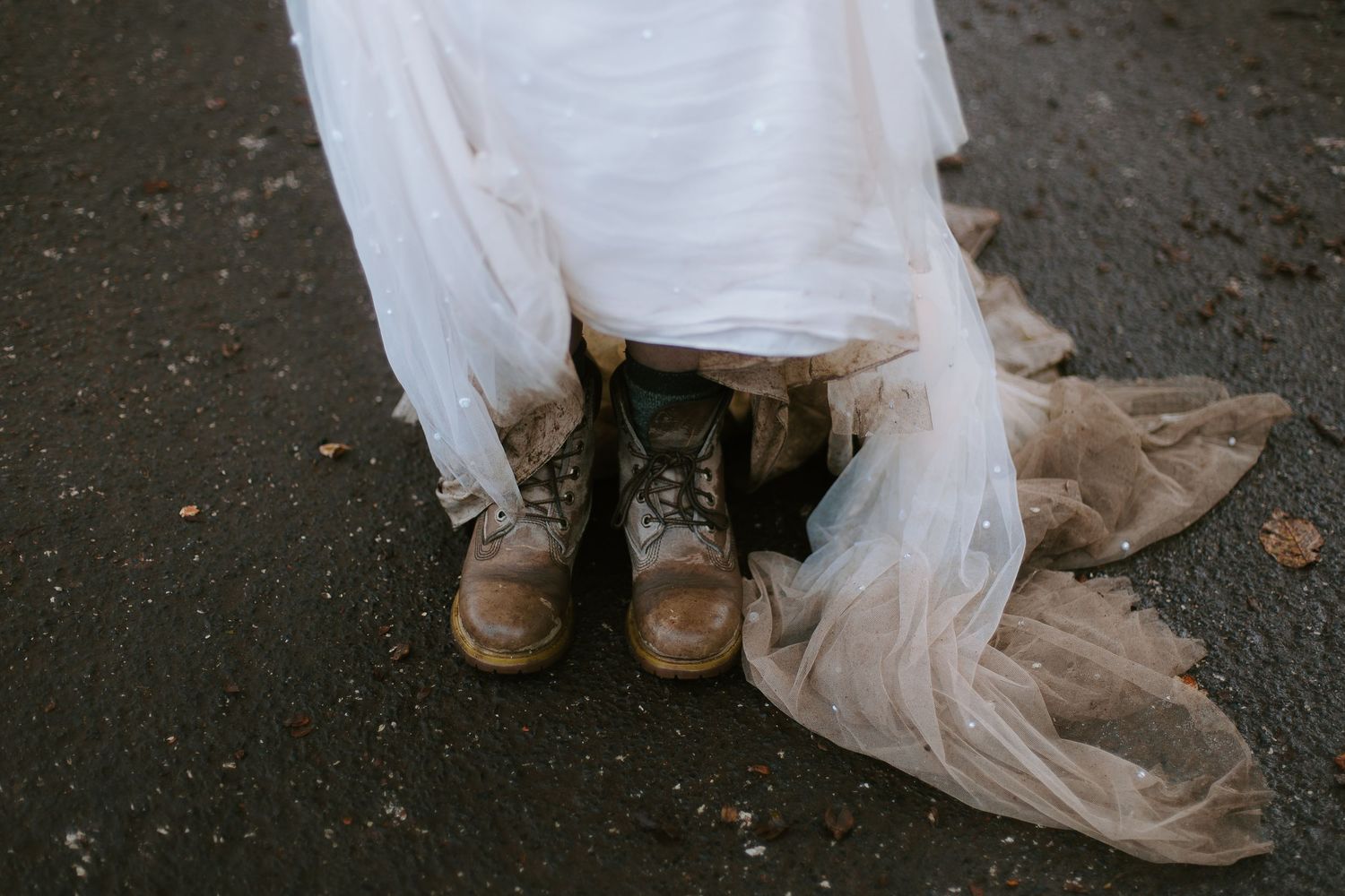 Brown leather boots peek out from beneath a flowing white wedding dress on a dark ground.