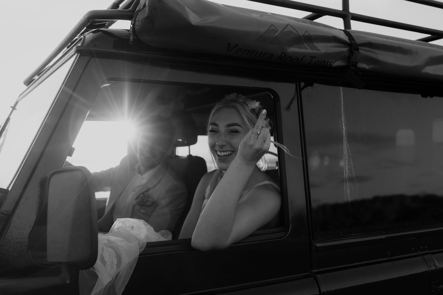 A car interior view shows someone in a white shirt driving while looking ahead through the windshield.