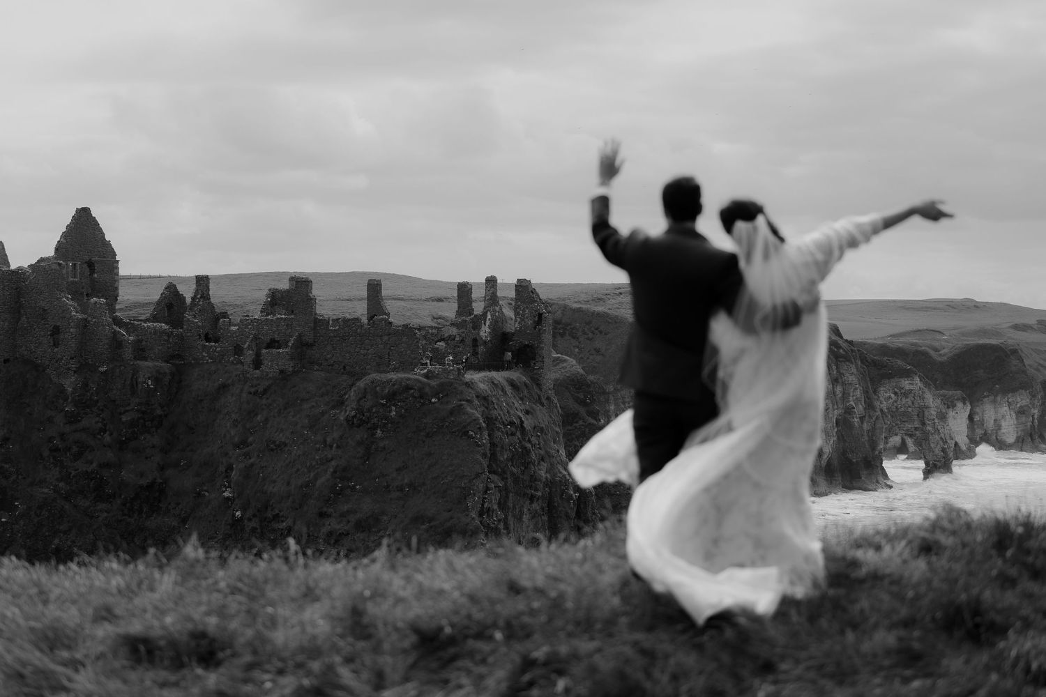 Wedding couple dances and celebrates on dramatic coastal cliffs.