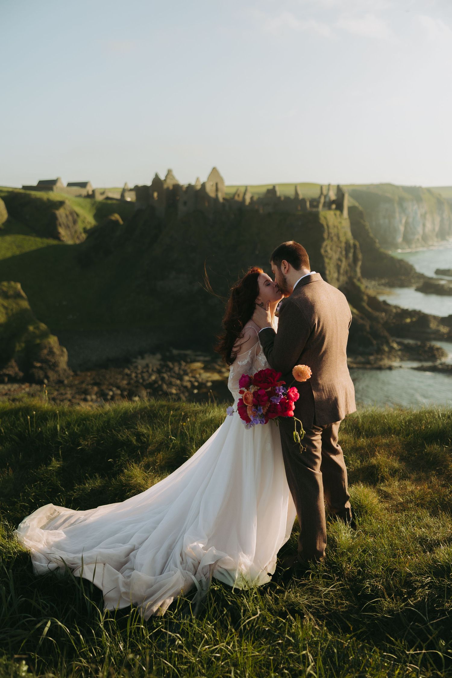 A couple shares a romantic moment on the cliffs of Dunluce Castle in Northern Ireland at sunset.