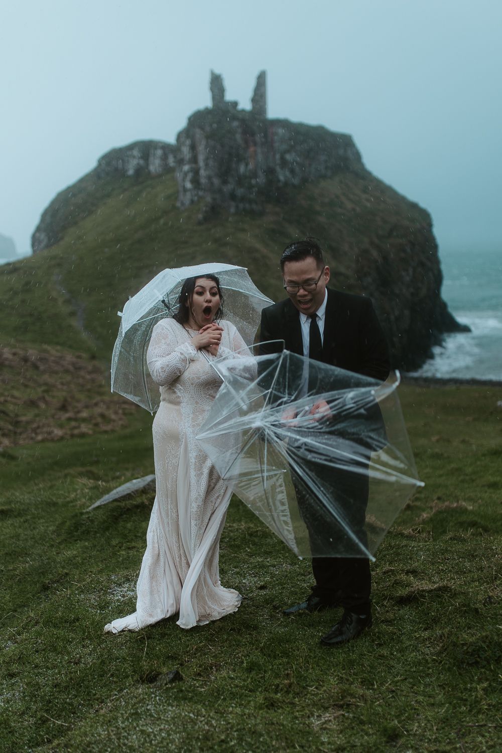 Wind blows through bridal attire during dramatic cliffside wedding shoot at coastal landmark ruins.