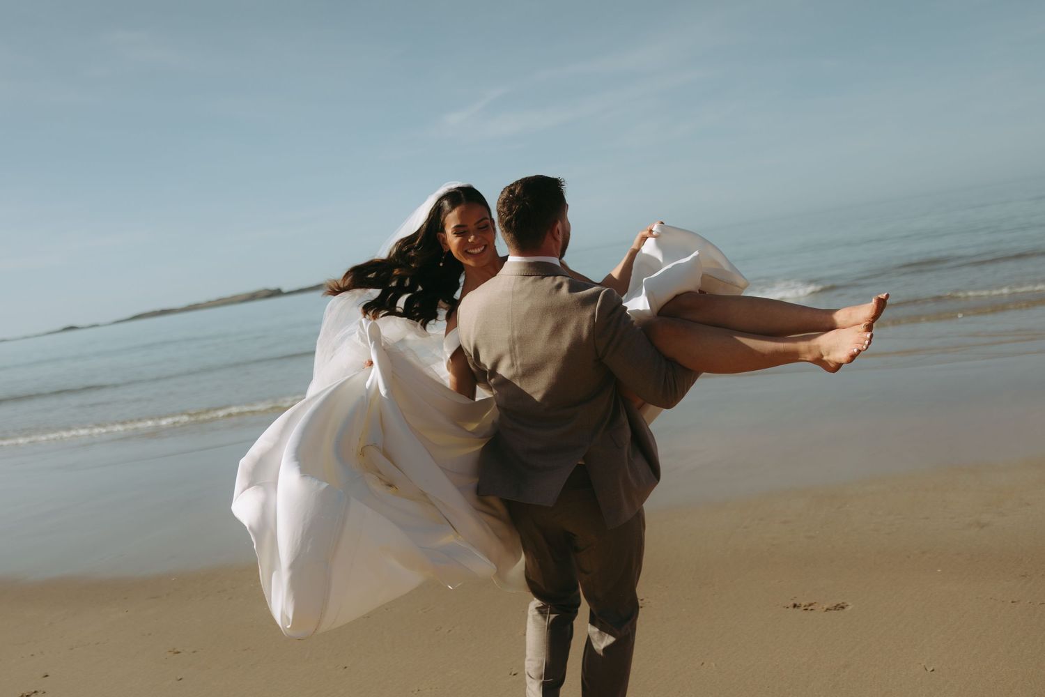 Romantic beach scene with couple in wedding attire by the ocean.