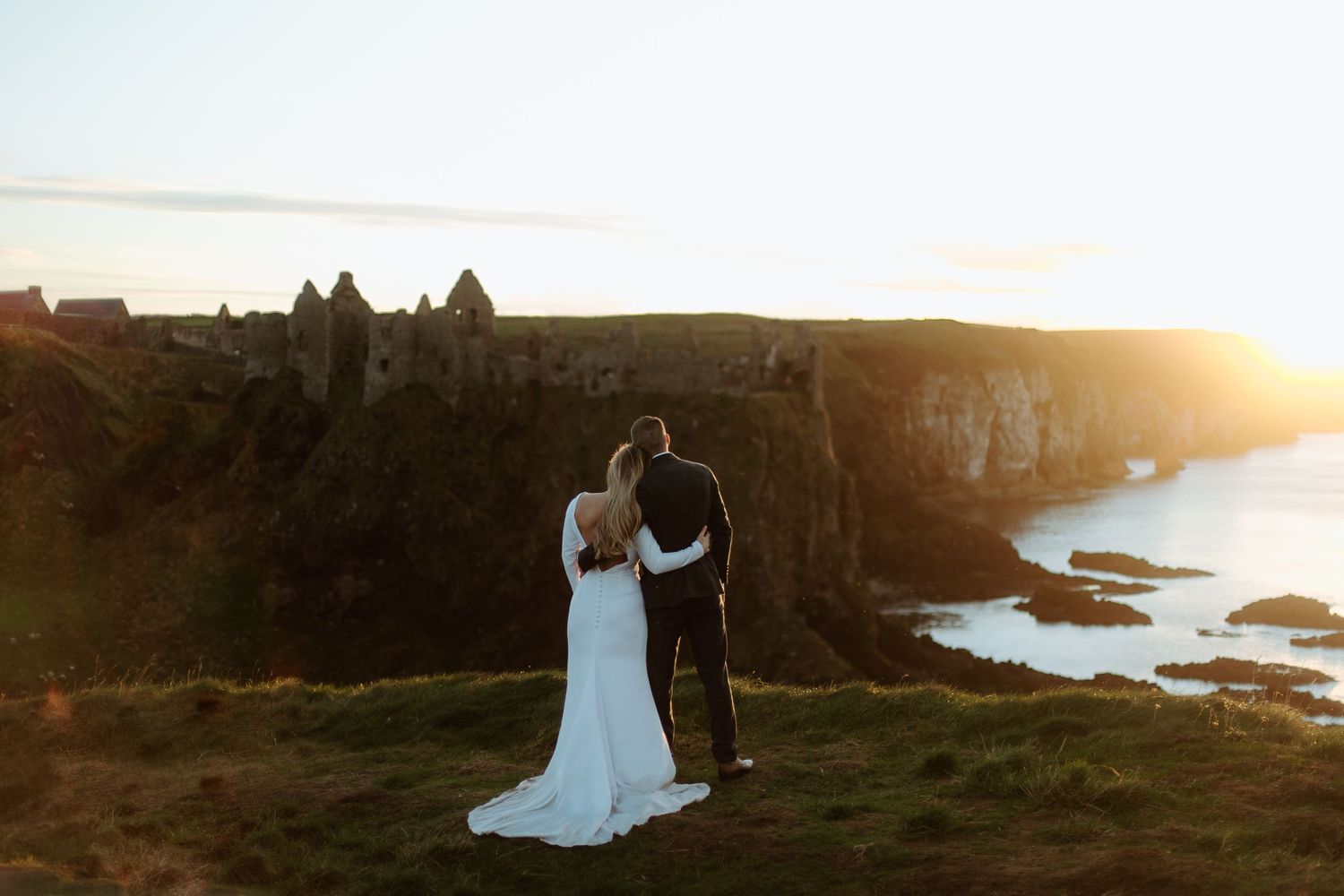 Silhouetted wedding couple standing on coastal cliffs during golden hour.