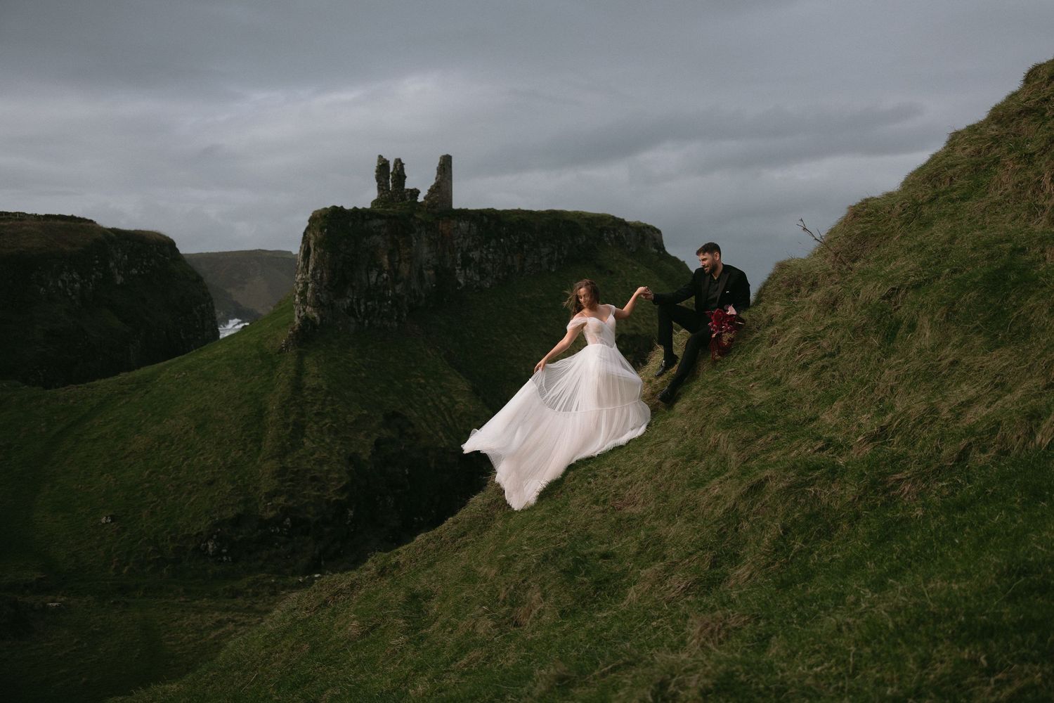 Dramatic cliffside wedding photography with moody overcast skies.