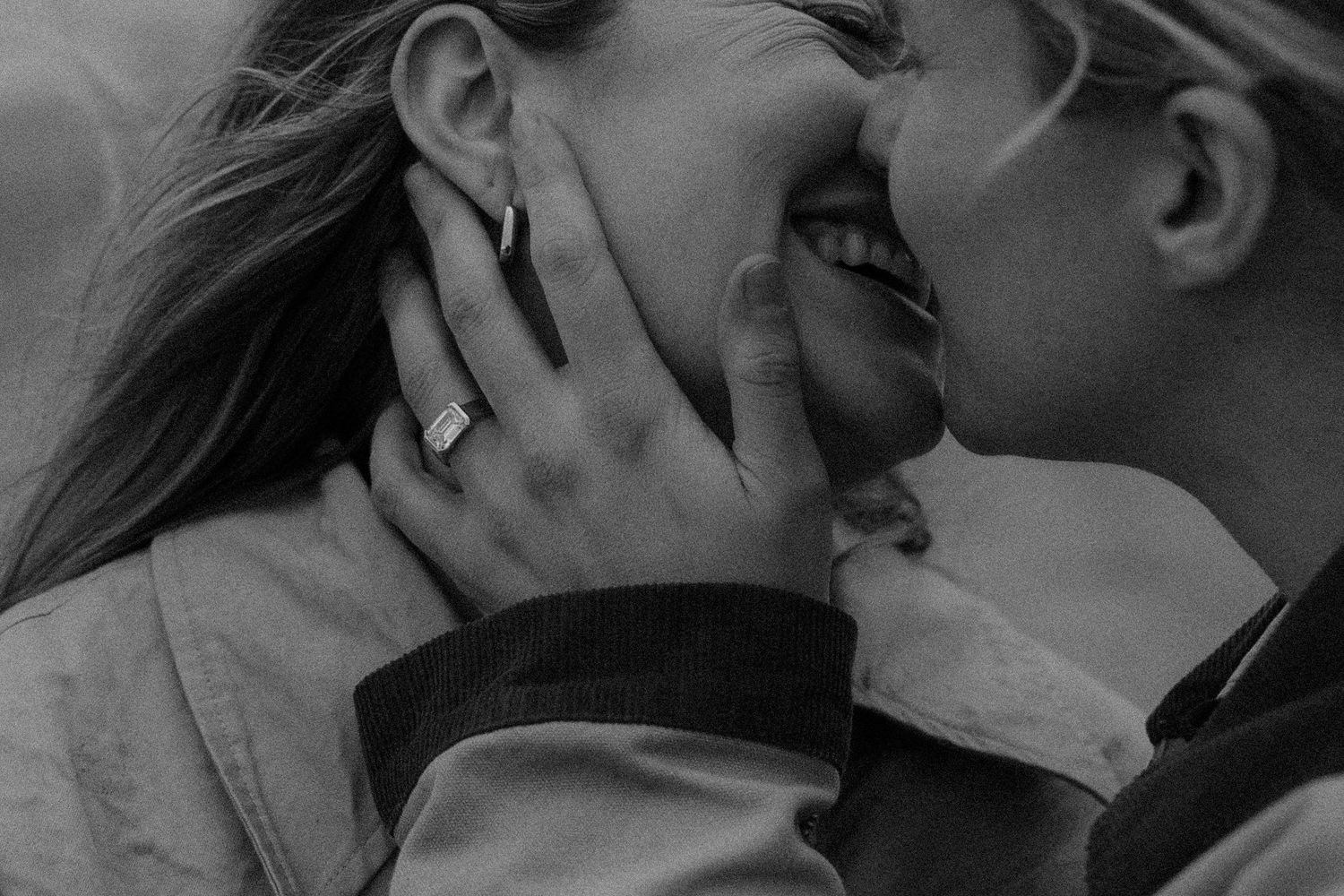 Black and white photo of a couple sharing a romantic kiss, woman wearing a ring, captured in intimate close-up.