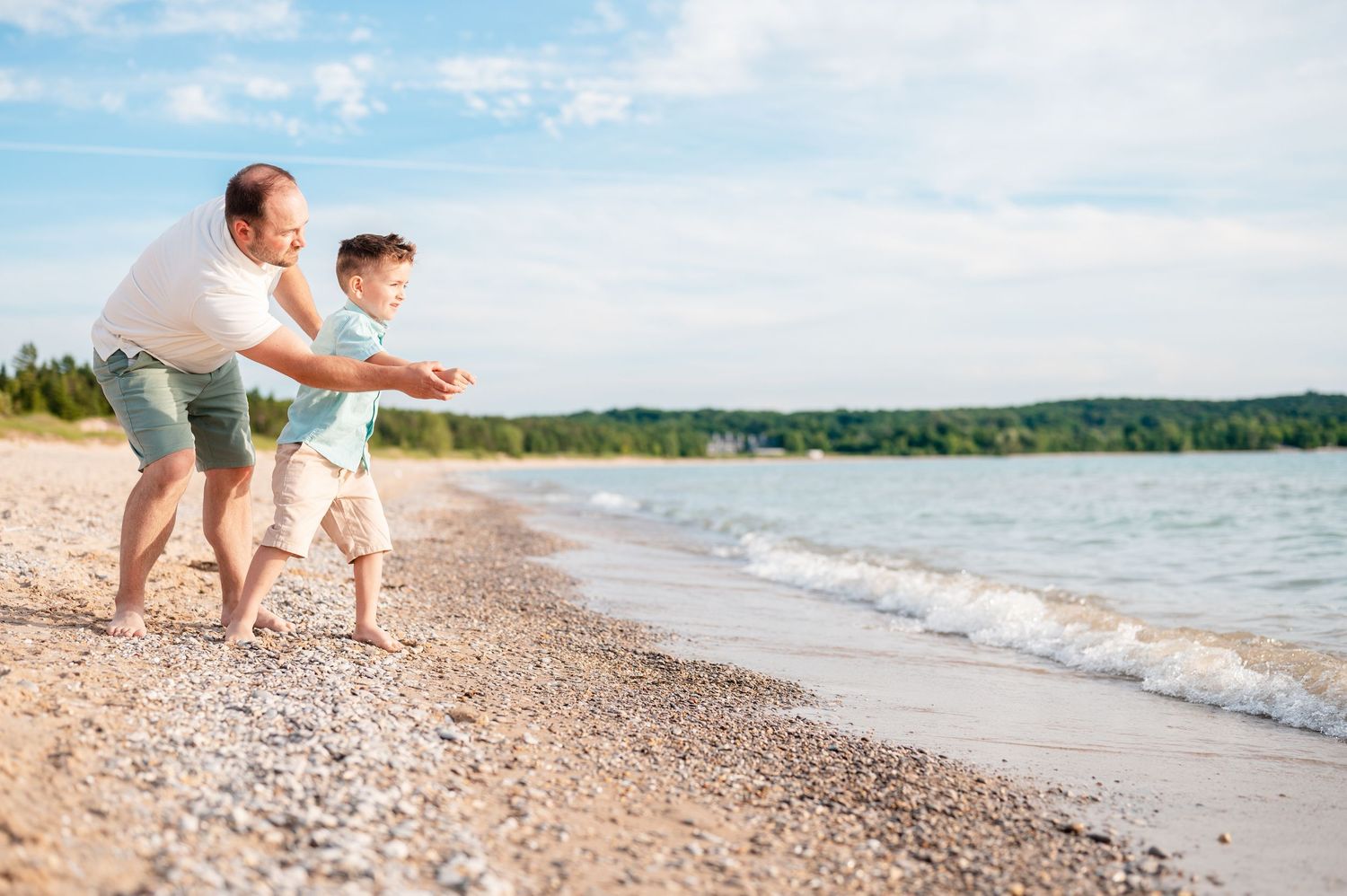 Father and son playing and splashing at the water's edge on a rocky beach.