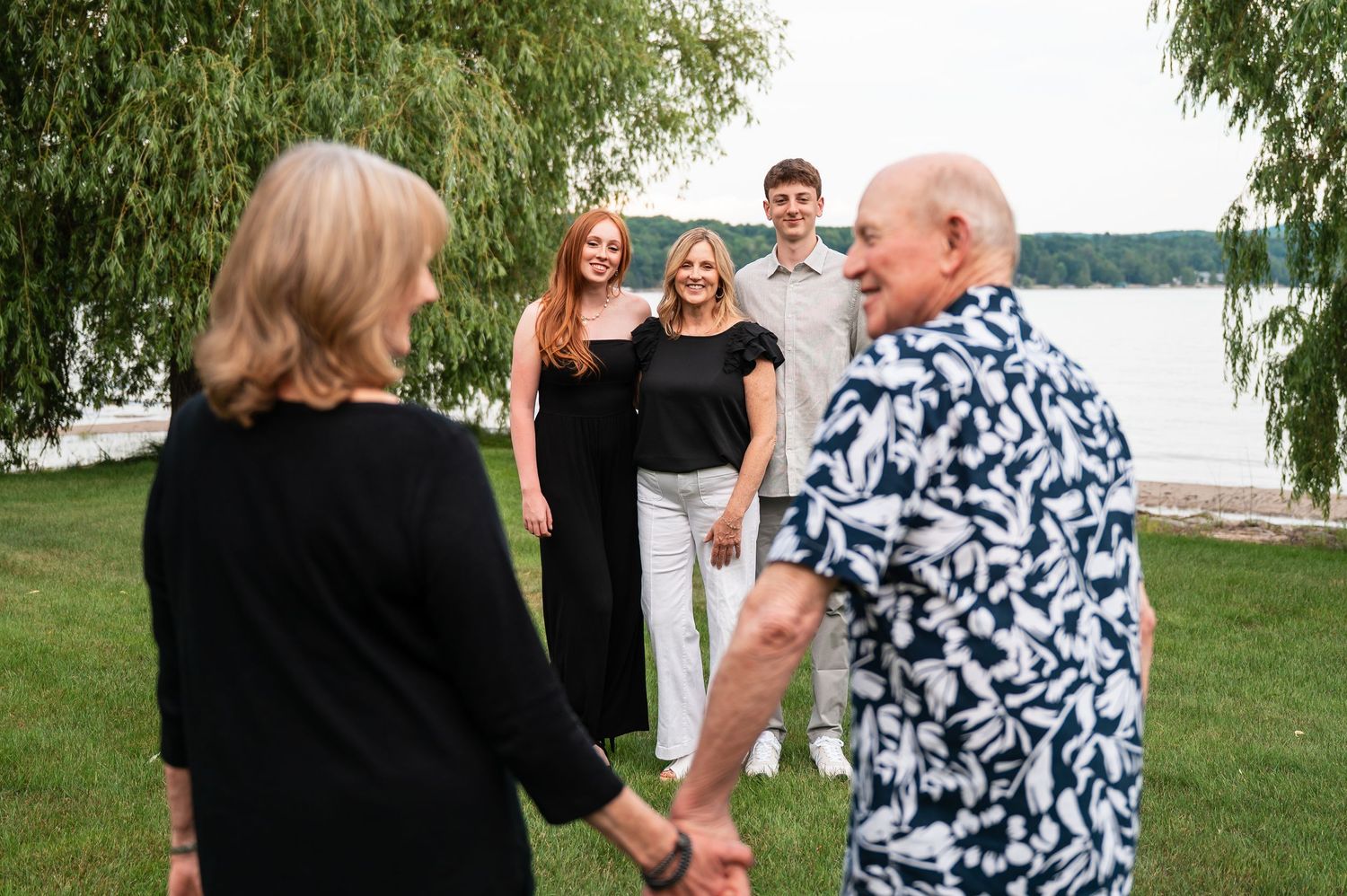 A small group gathers on a lawn by a lake during a casual outdoor gathering.