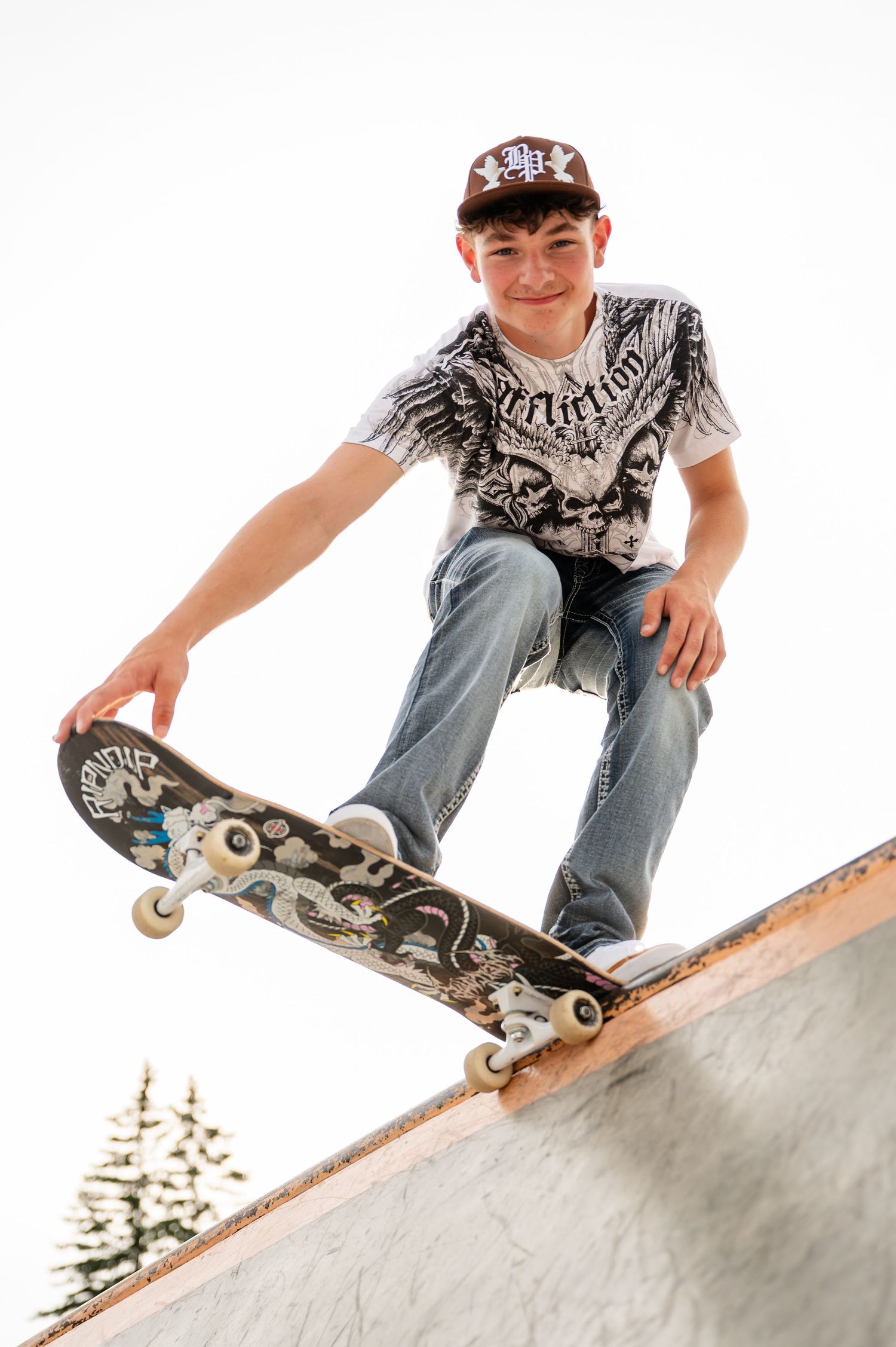 Skateboarder performs trick on ramp wearing patterned t-shirt and  cap.