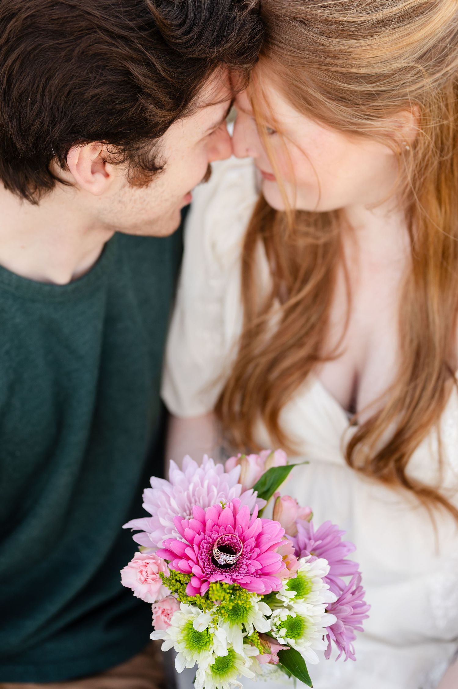 Pink and white flowers in focus with a romantic couple embracing in soft focus behind them.