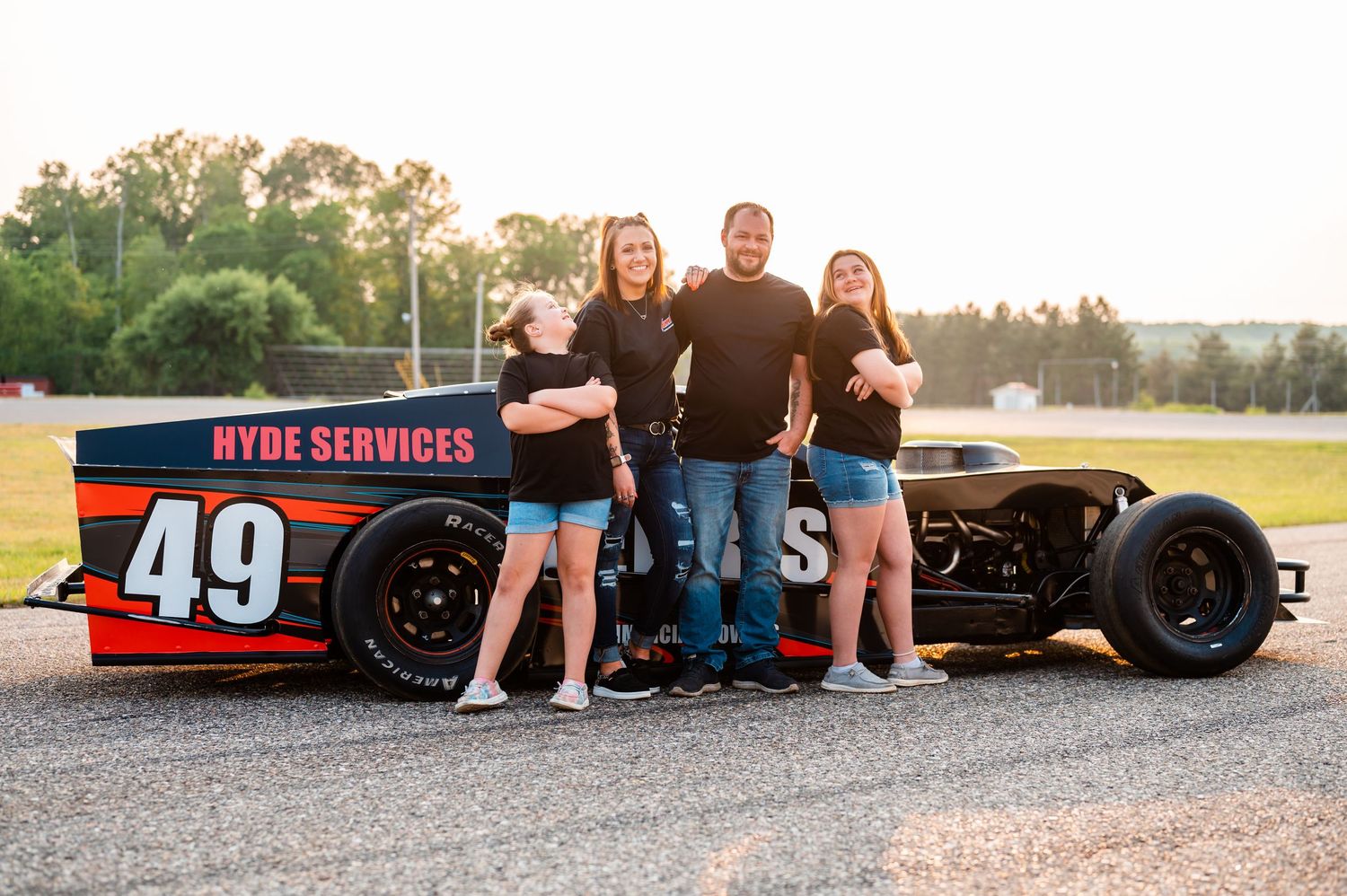 Family poses beside a black racing car.