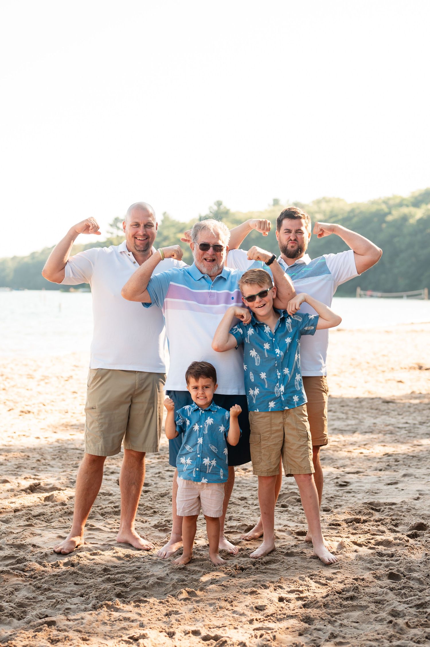 Family members flexing muscles playfully on sandy beach at sunset.
