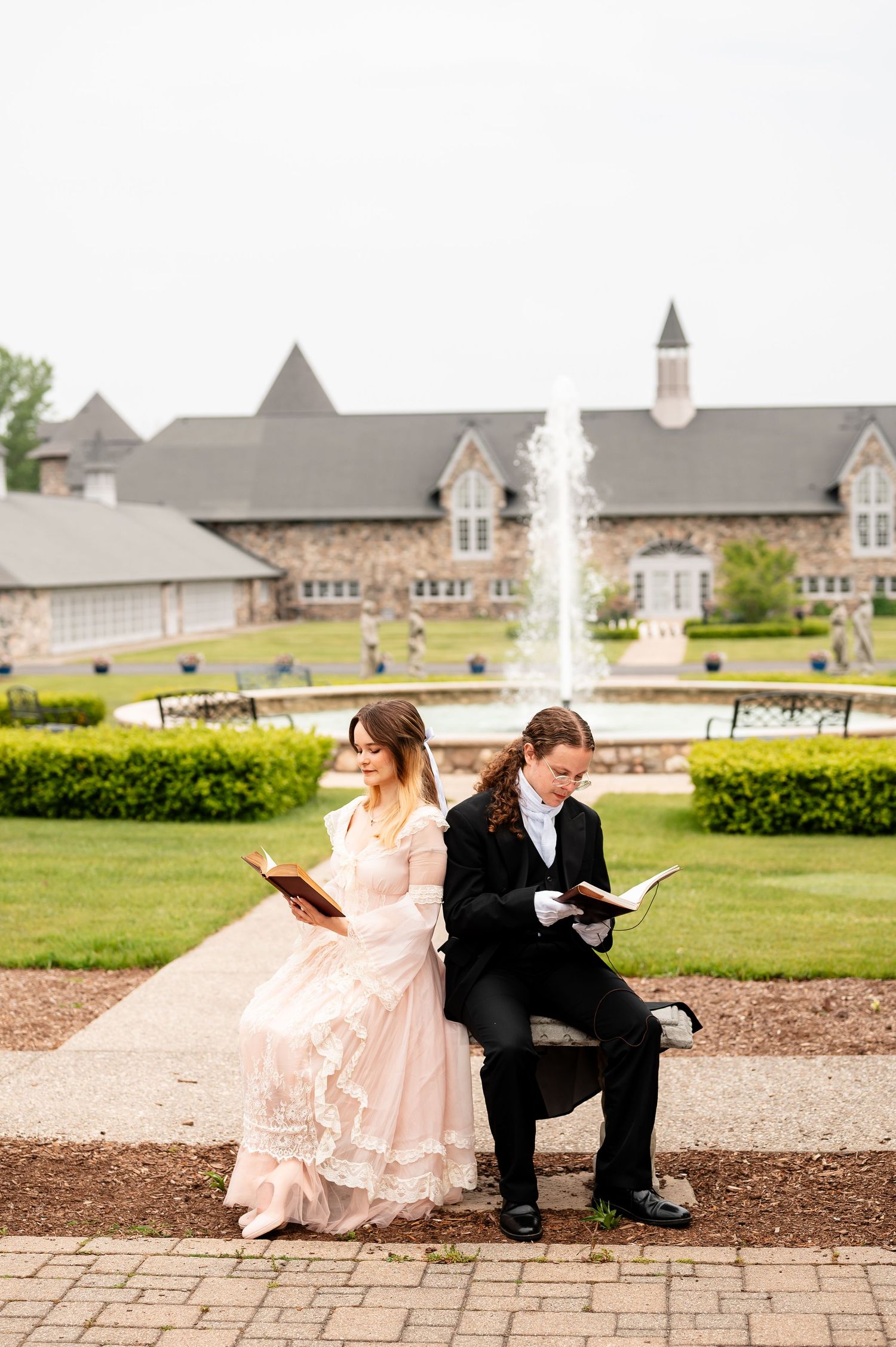 Couple in formal attire shares playful moment on stone path near fountain.