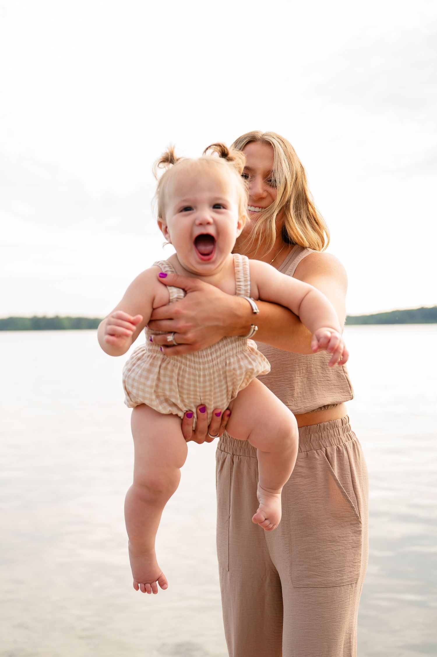A playful moment captured by the lake with a baby wearing a ruffled romper and mother swinging her forward,