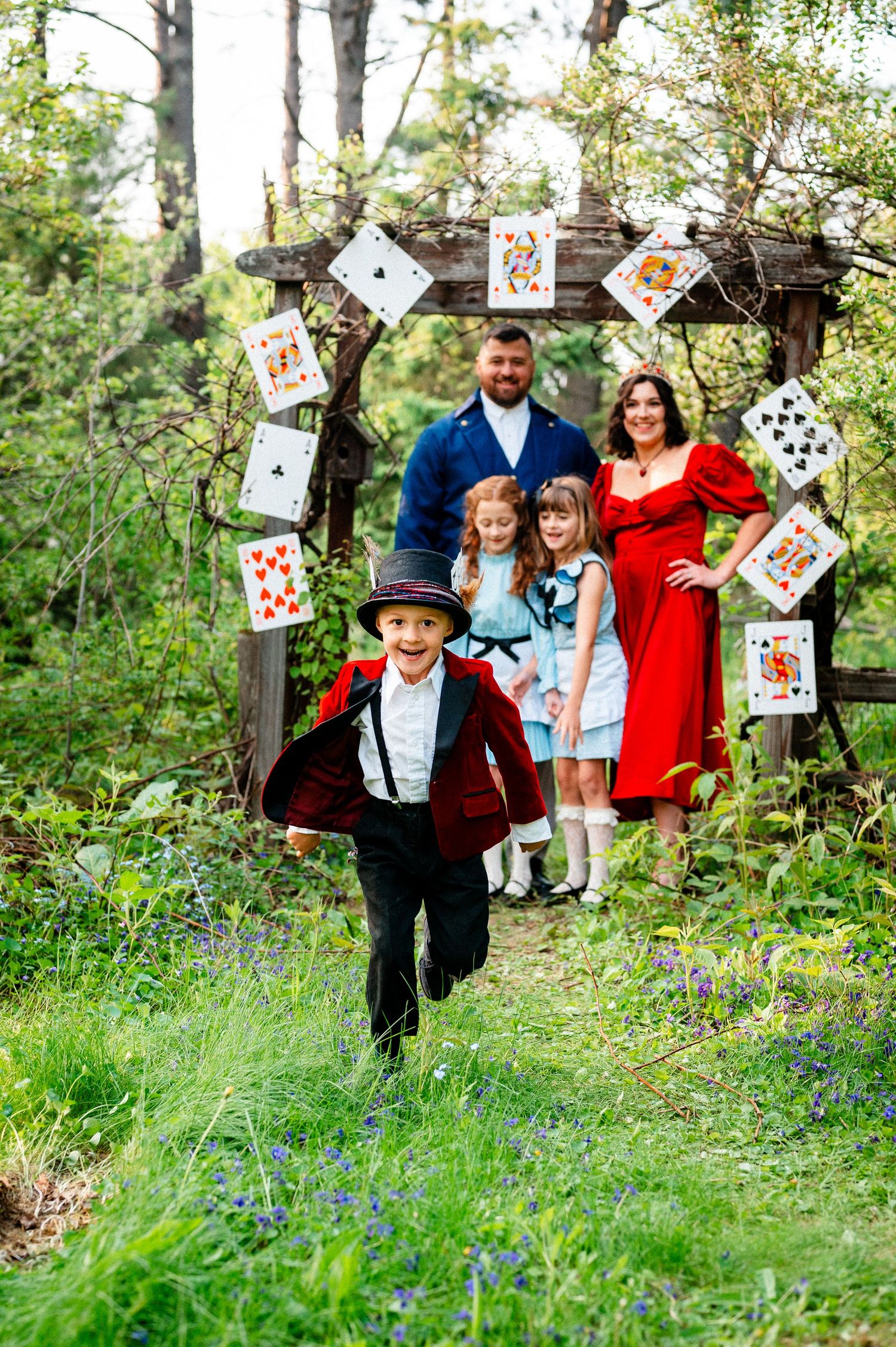 Whimsical family photo with playing cards decorating trees in a forest setting.