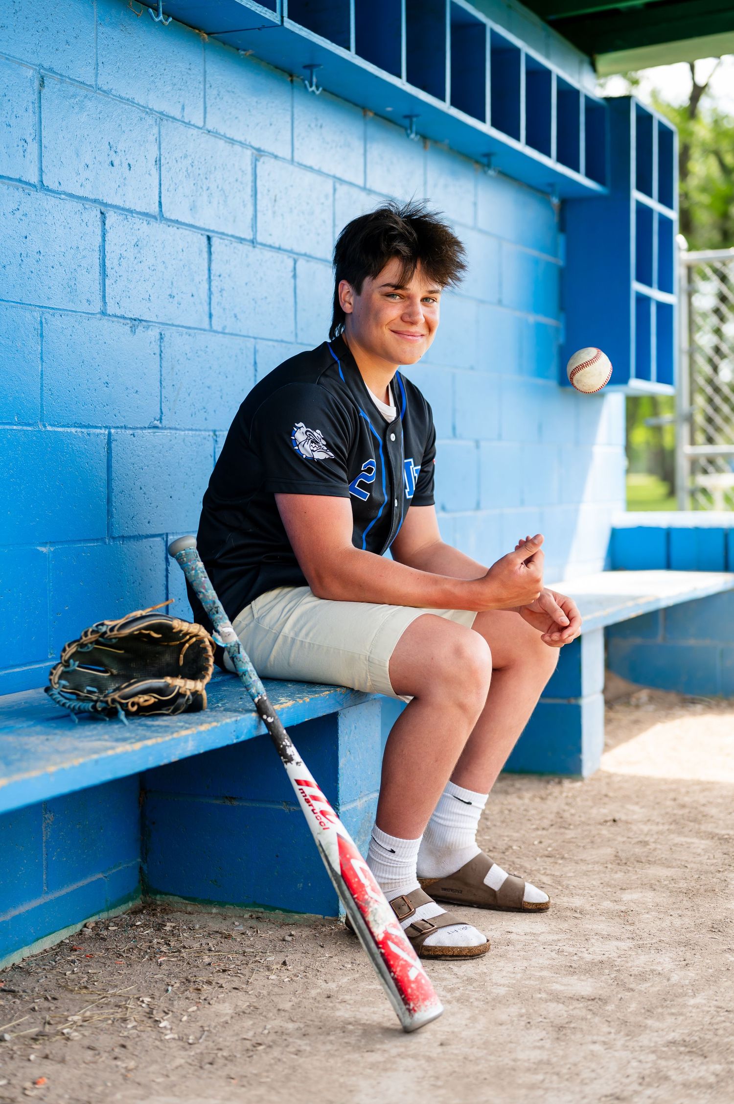 Baseball equipment rests on a dugout bench against bright blue painted walls.