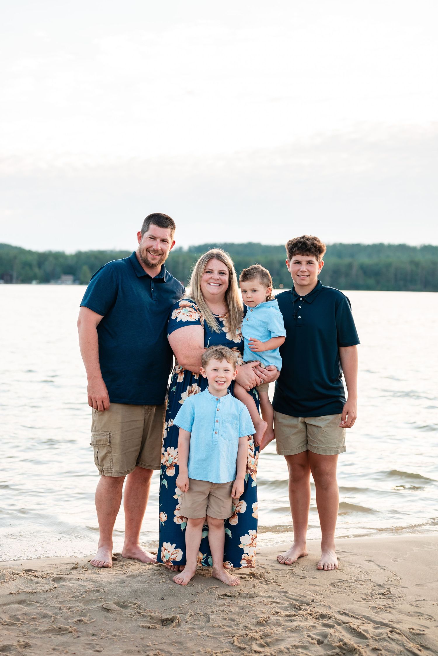 Family enjoying a sunset beach photoshoot together in coordinated blue and khaki outfits.