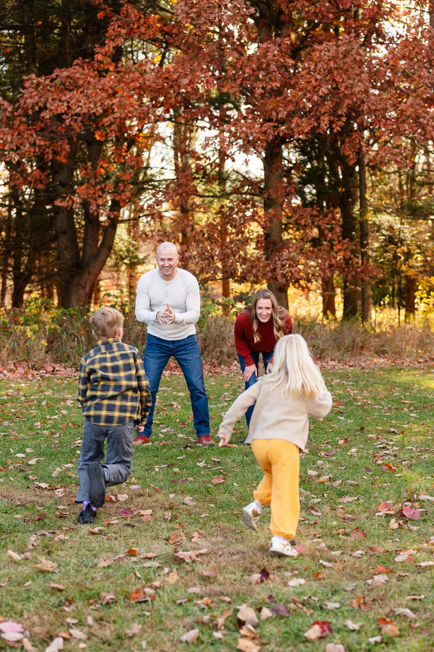 Family playing and running through fallen autumn leaves in wooded park setting.