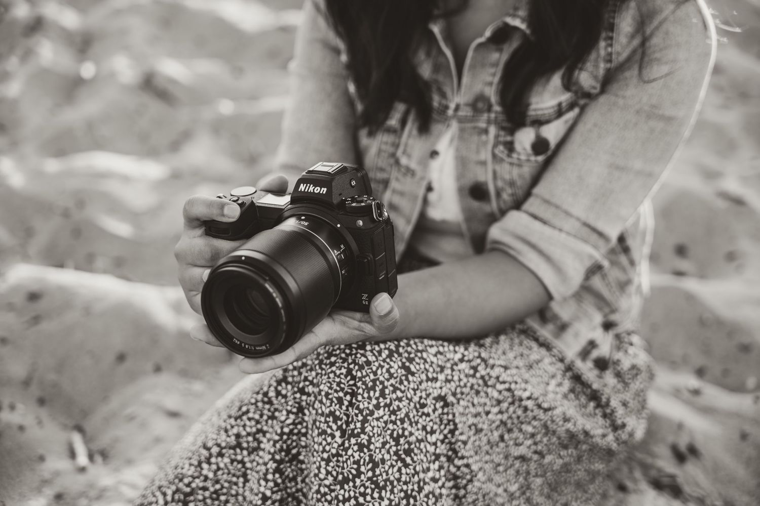 Black and white portraits of a photographer with camera sitting on sand.