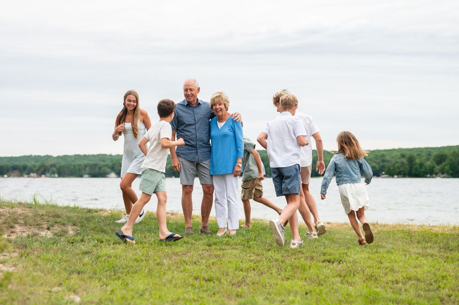 Grandchildren are running around grandparents by the lake on a overcast day.