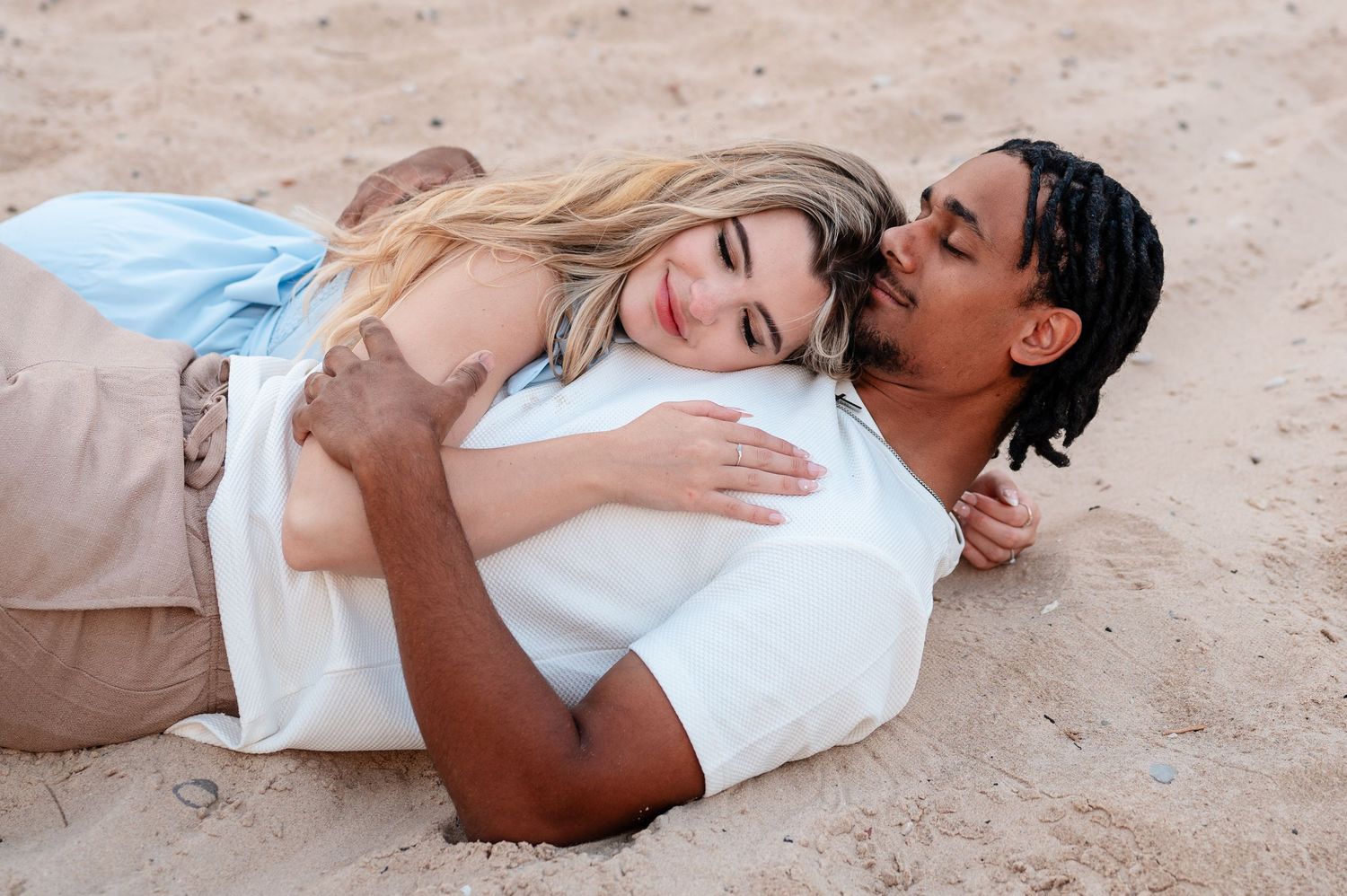 Couple lying together on sandy beach during engagement photoshoot.