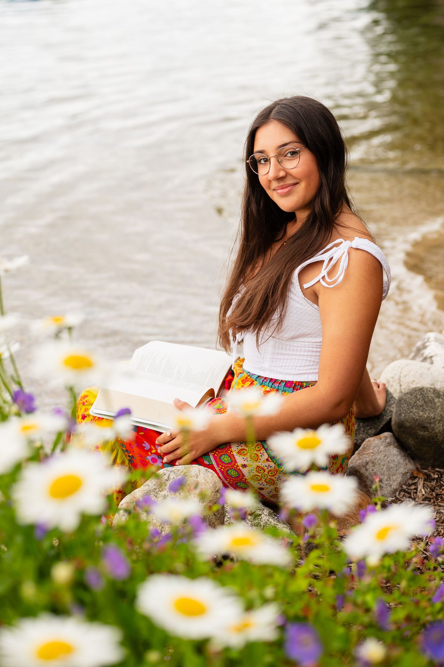 White daisies bloom in the foreground near a peaceful waterfront setting.