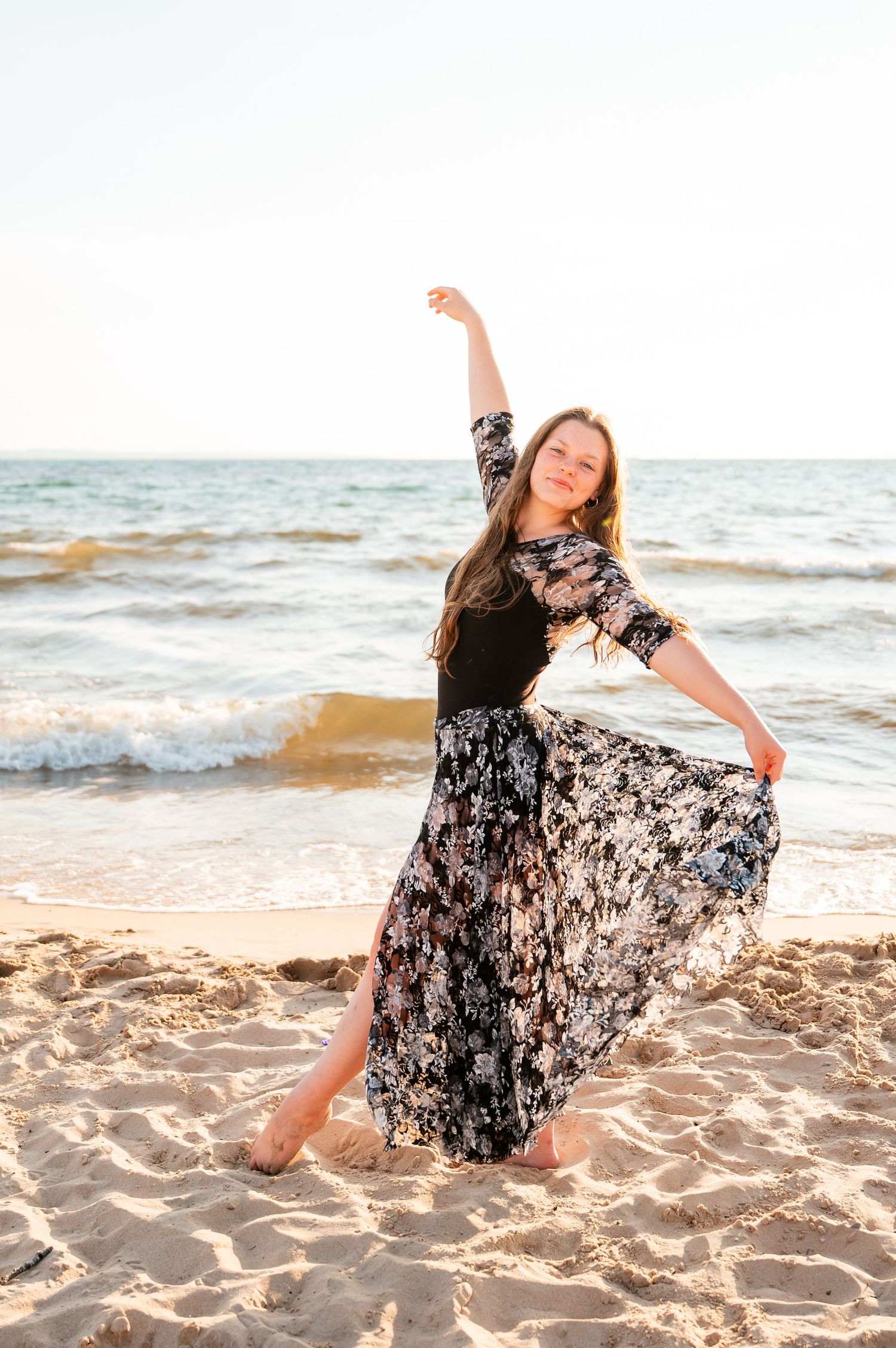 Joyful dance pose on beach at sunset in flowing floral dress.