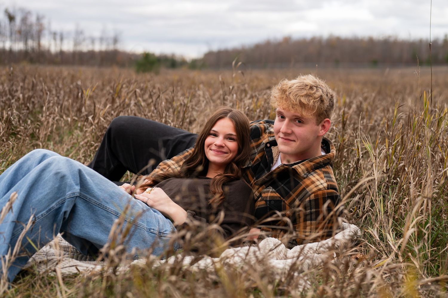 Couple lying in tall autumn grass during an outdoor photo session.