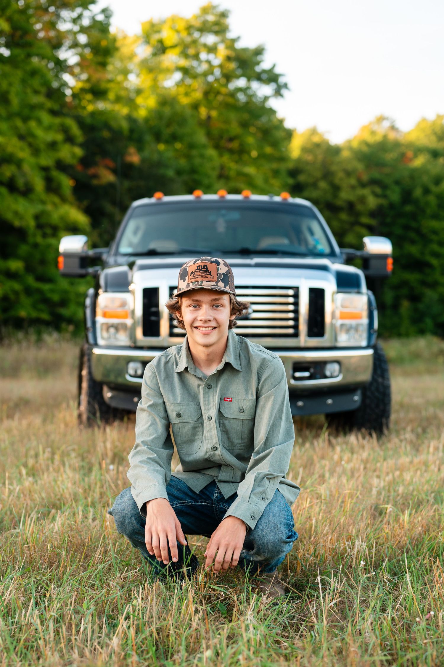 Outdoor portrait session in a grassy field with pickup truck in the background during golden hour.