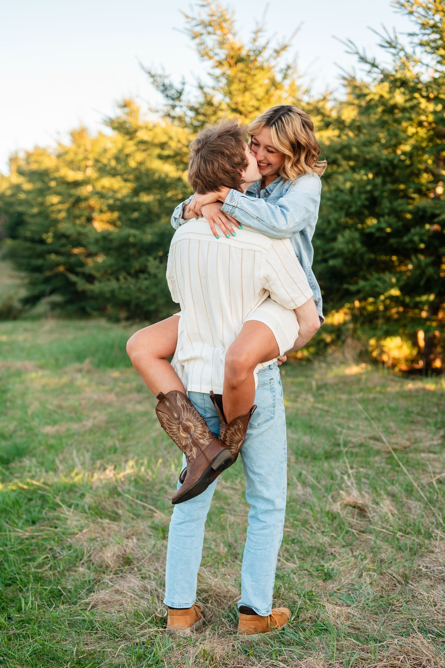 Couple in denim and white clothing embraces in a golden field at sunset.
