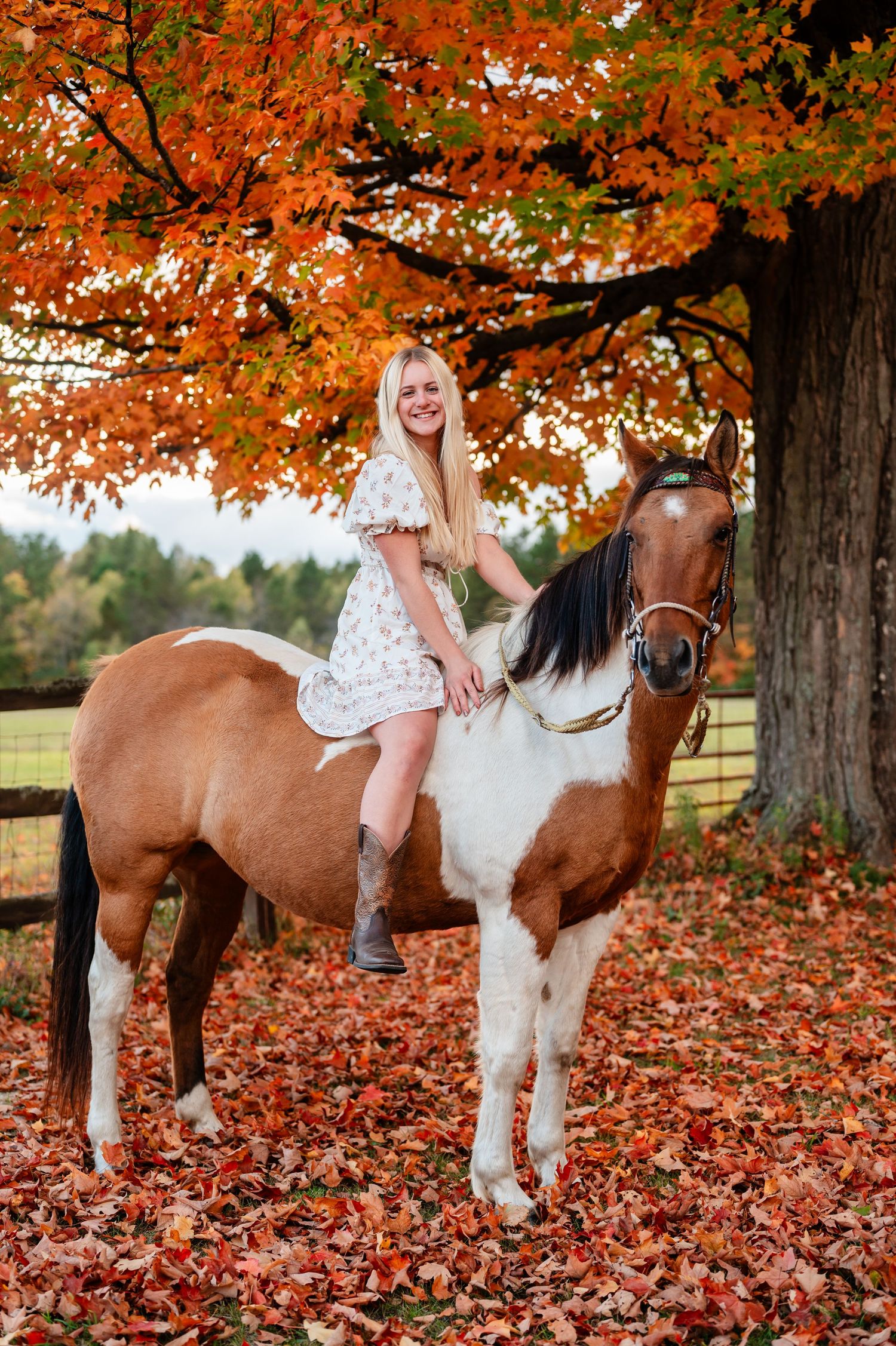 Senor girl riding brown and white horse under orange fall foliage.