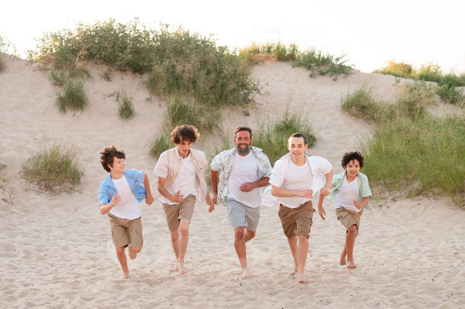 Father and sons running and playing together on a sandy beach at sunset at the dunes in Petoskey Michigan.