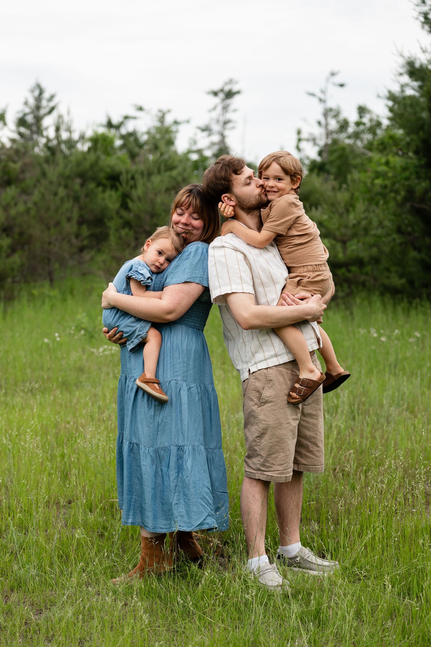 Sweet family embraces and hugs in a grassy location.