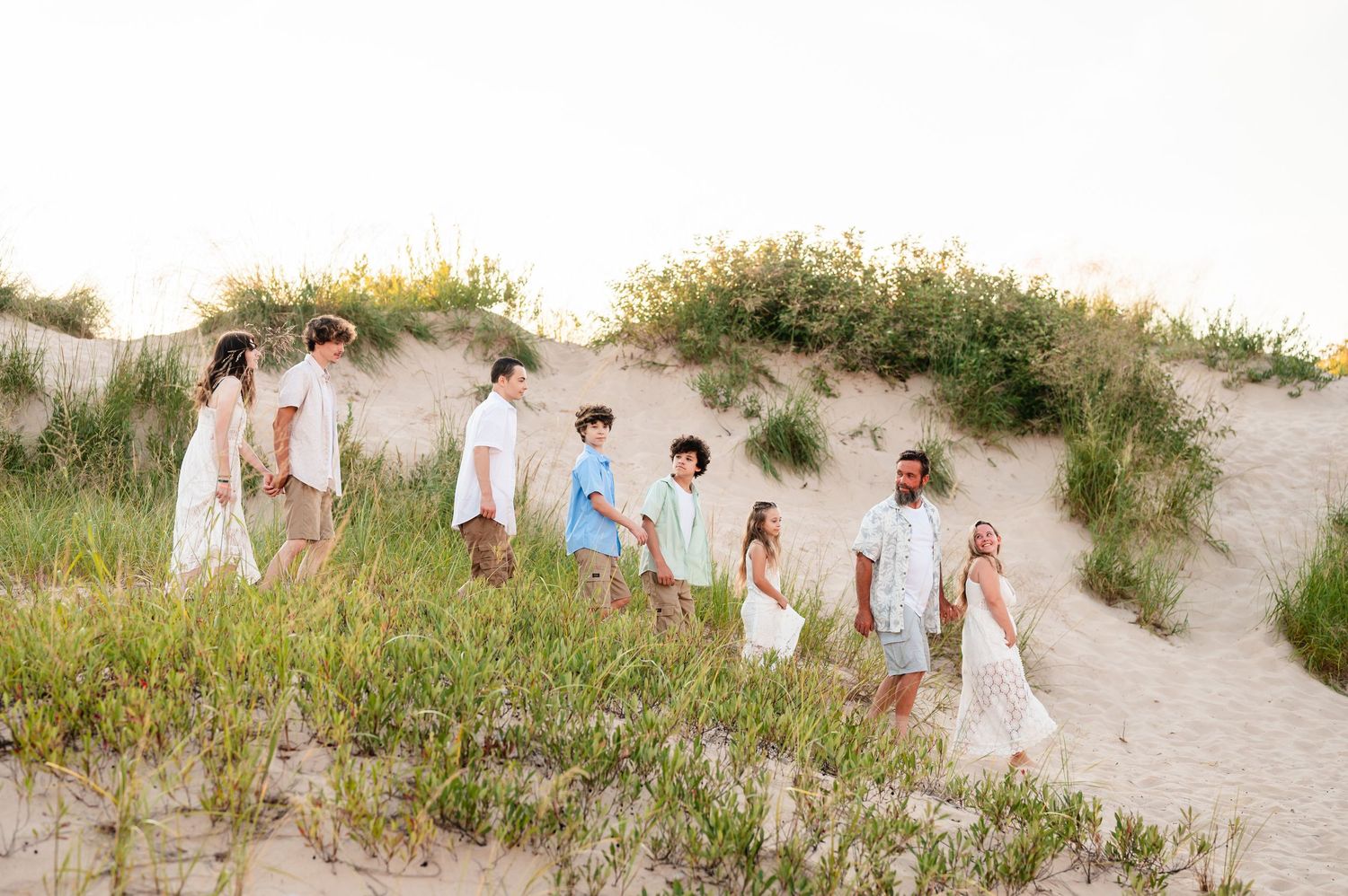 Family session follow the leader on sandy dunes at beach wearing coordinated neutral summer outfits.