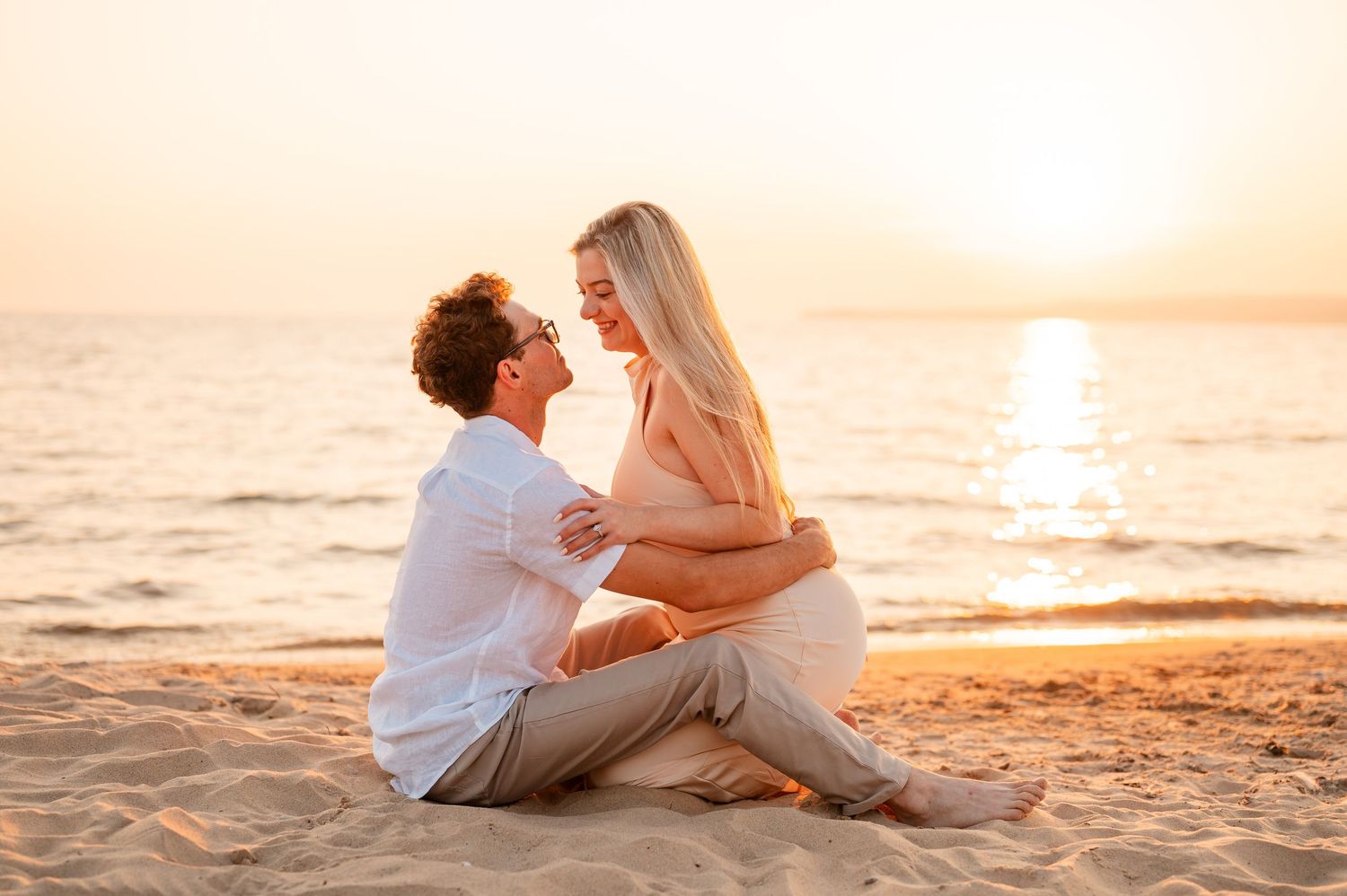 Couple sharing intimate moments on sandy beach during golden hour sunset.