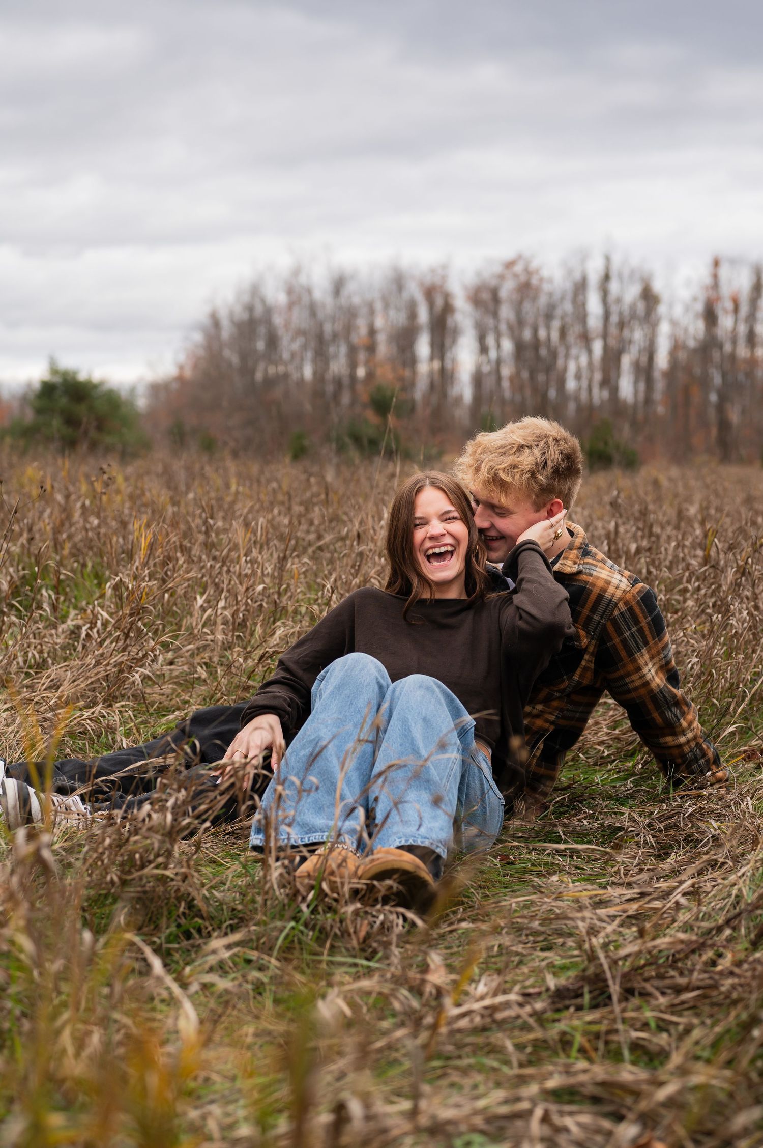 Candid moment of couple laughing while lying in a field of dried grass.