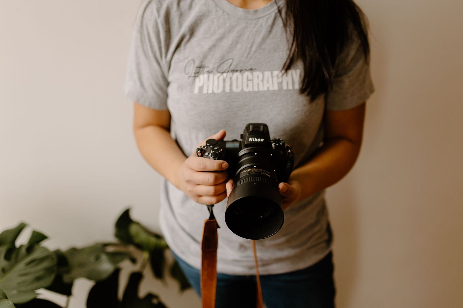 Close up of hands holding professional camera while wearing photography themed shirt.