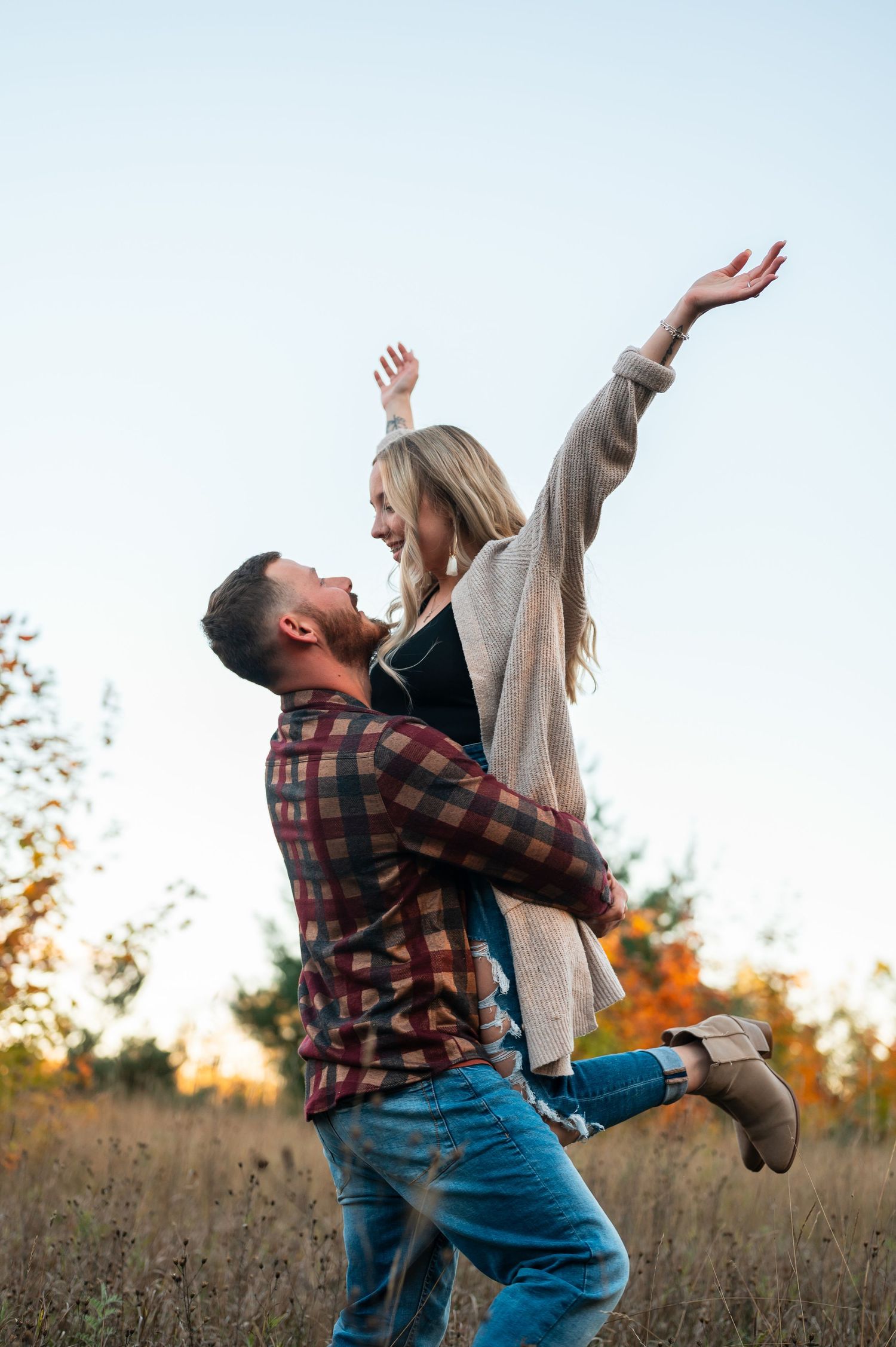 A couple shares a joyful moment as one lifts the other in an autumn field in Gaylord, MI