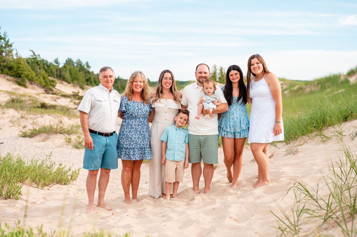 Extended family group poses together on sandy beach dunes in summer wearing shades of blue.