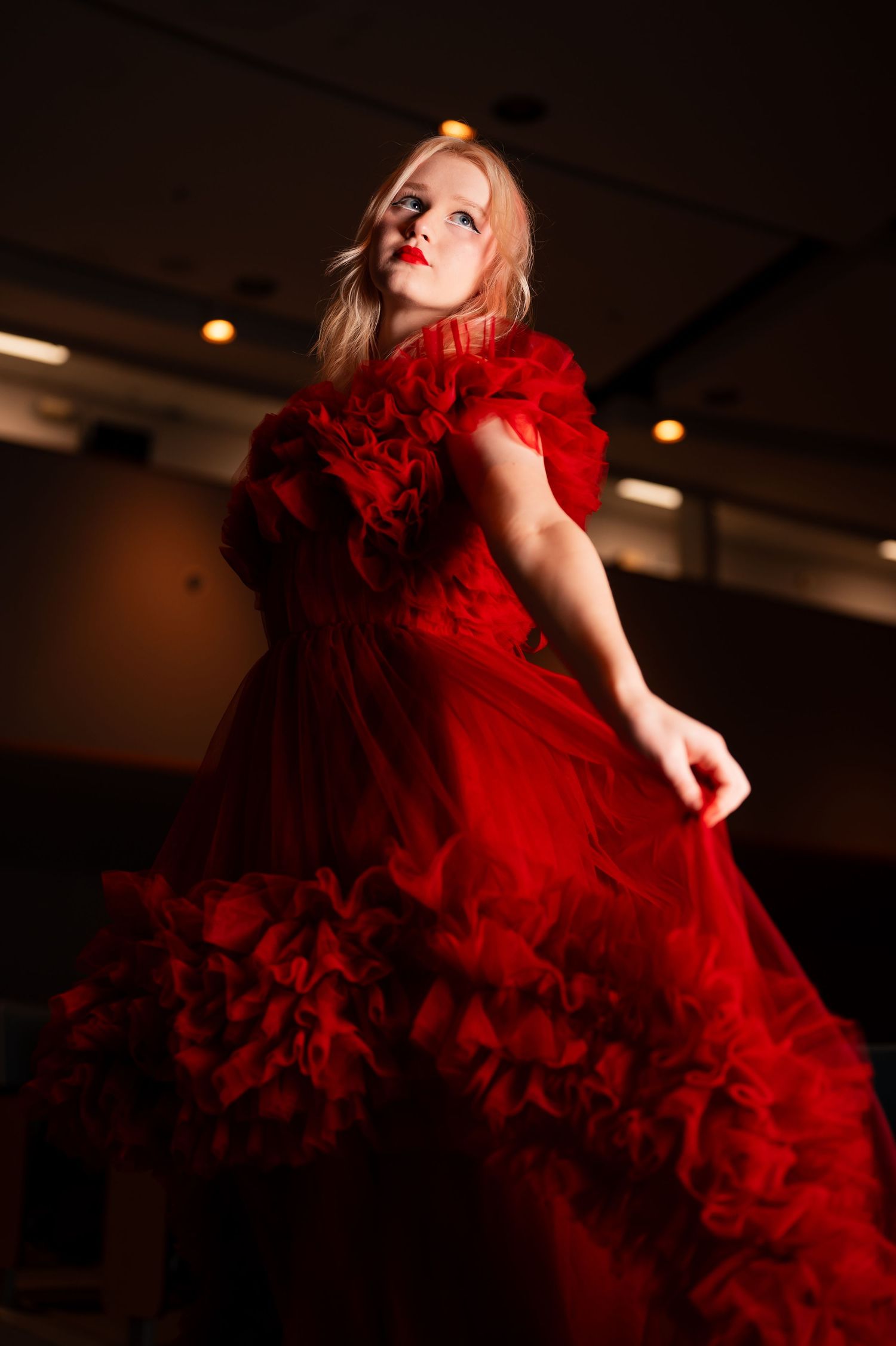 Dramatic portrait of a senior girl in flowing red gown against dark background. Lights, camera action.
