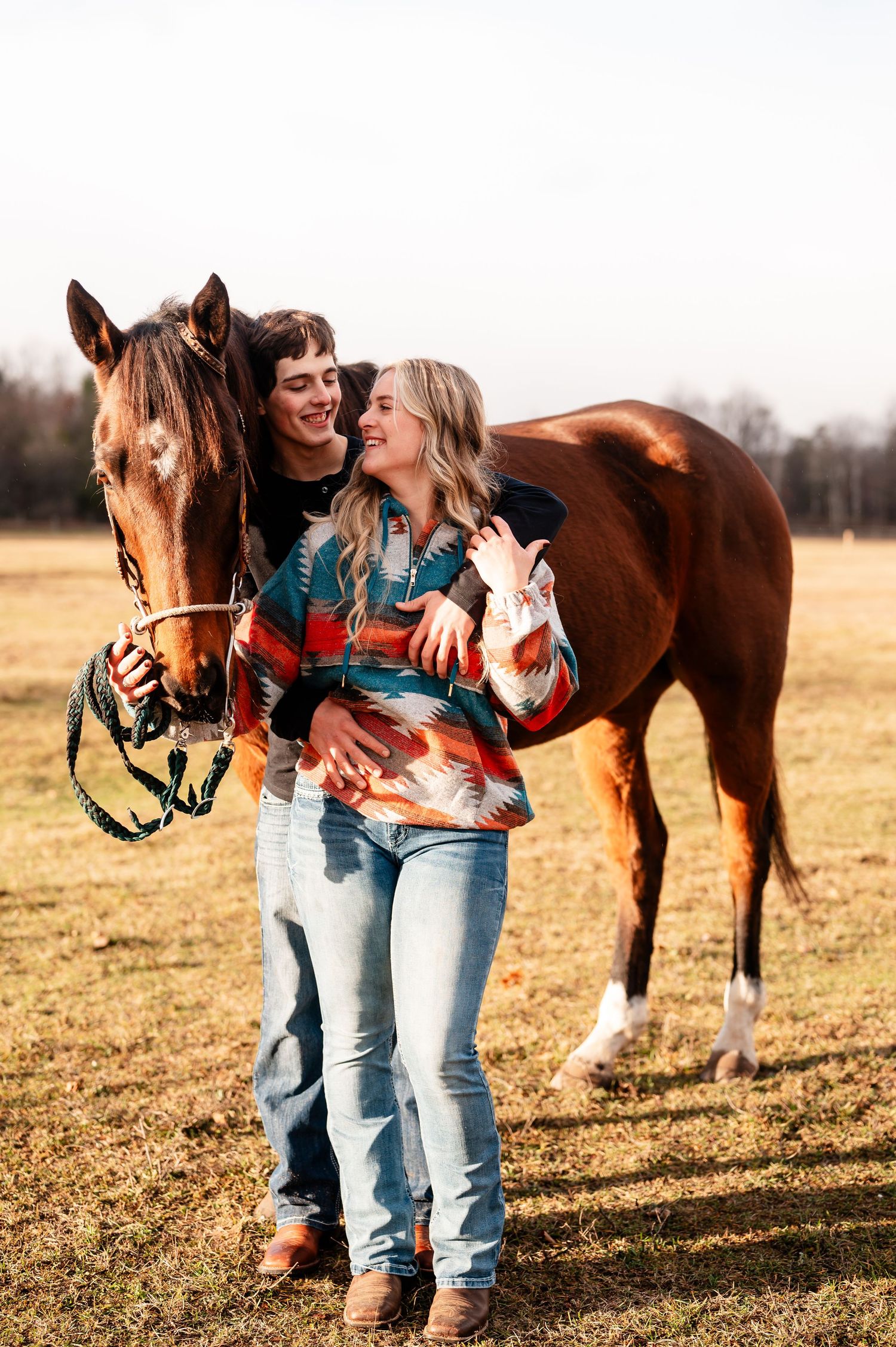 Couple in casual wear shares intimate moments with horses in a sunlit field.