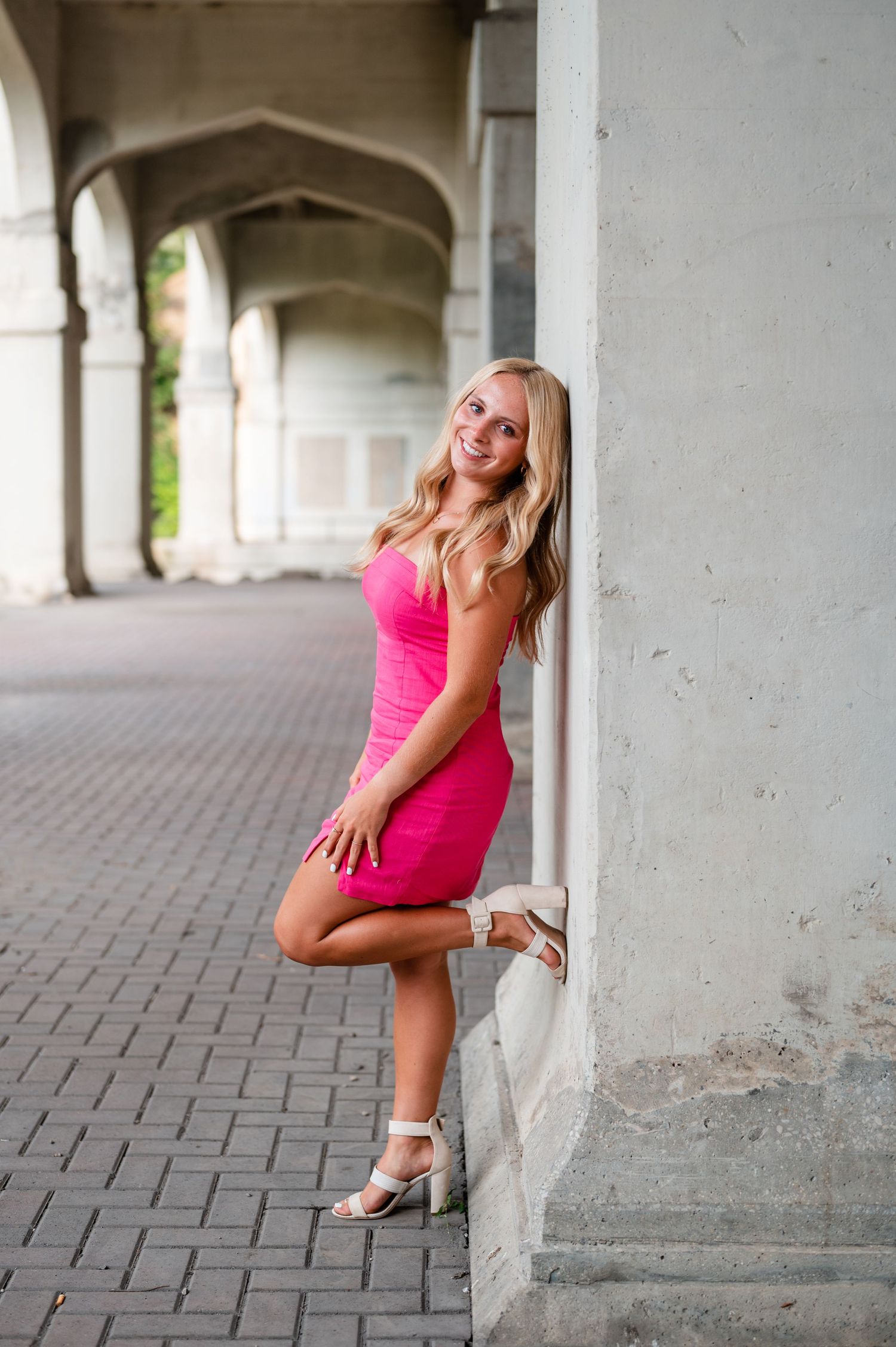 Girl in pink dress posing playfully against white pillared architecture.