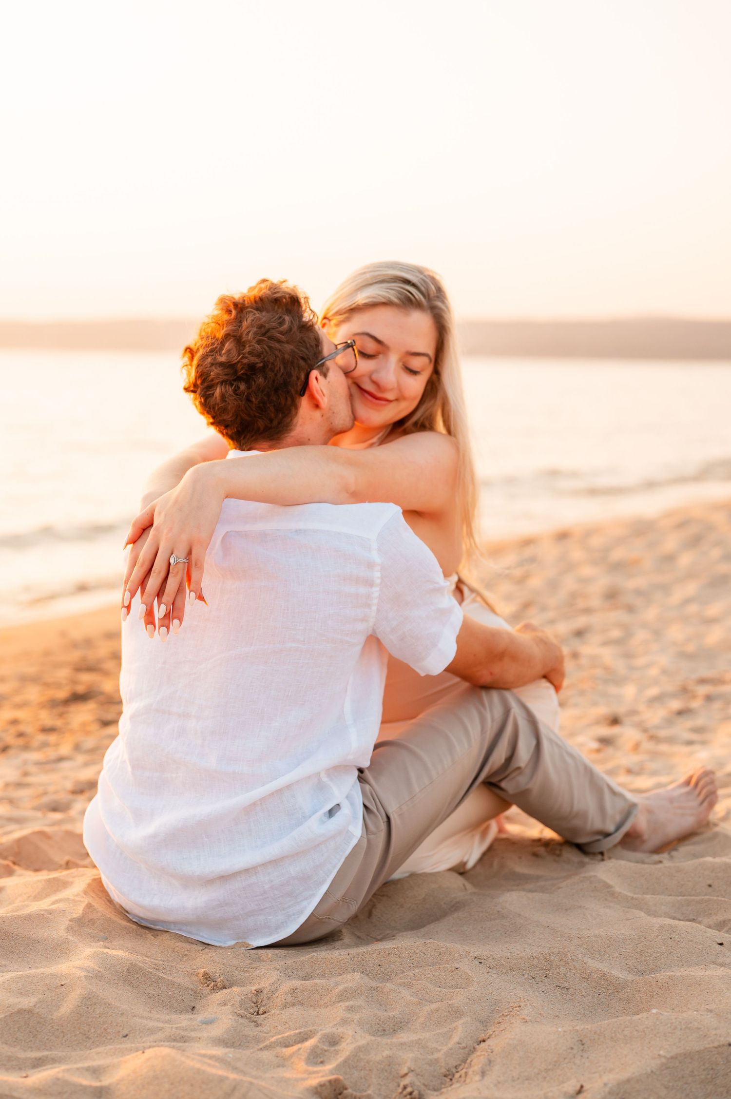 An engagement session for a couple that sits together on a sandy beach at sunset creating an intimate silhouette.